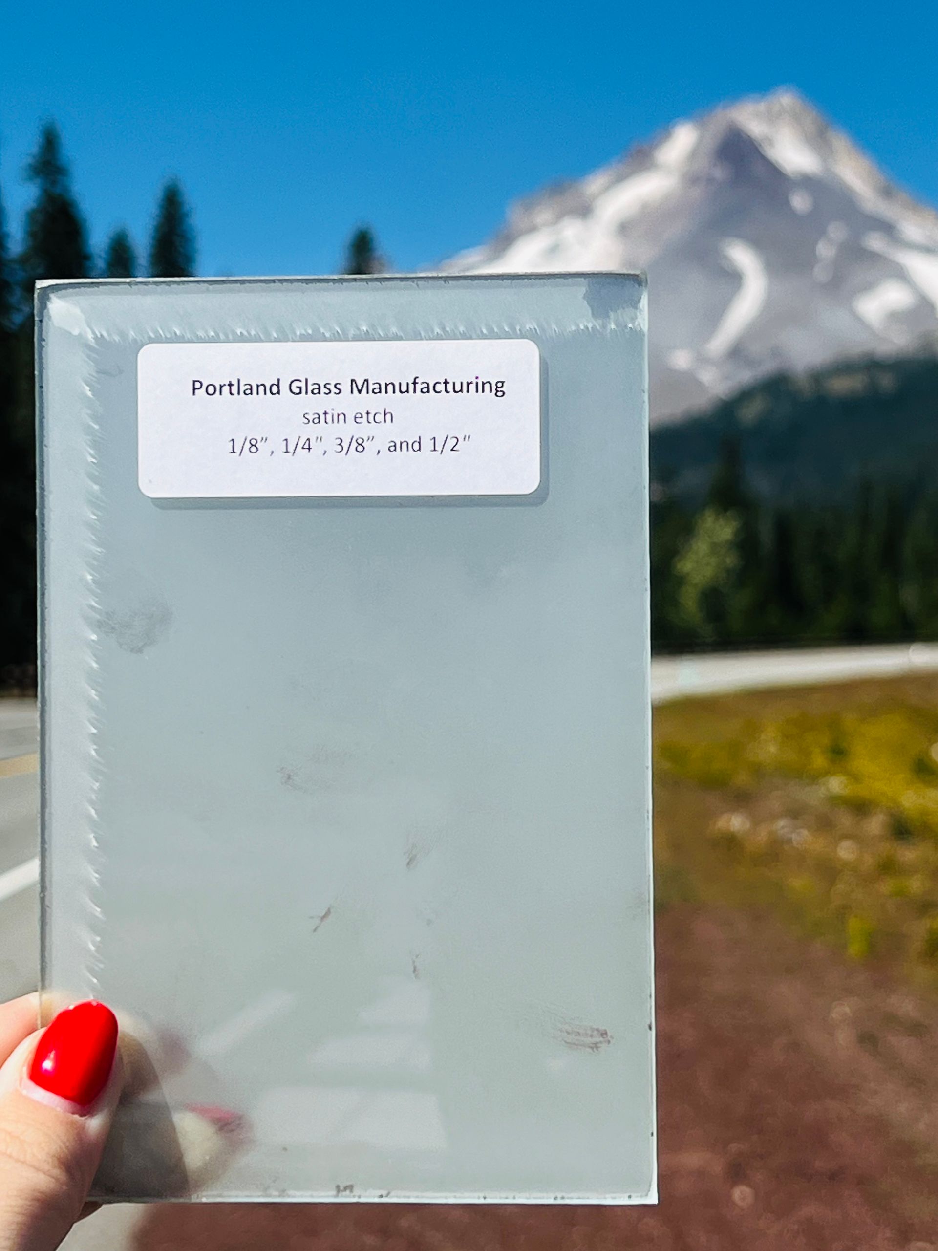A person holding a piece of glass with a mountain in the background