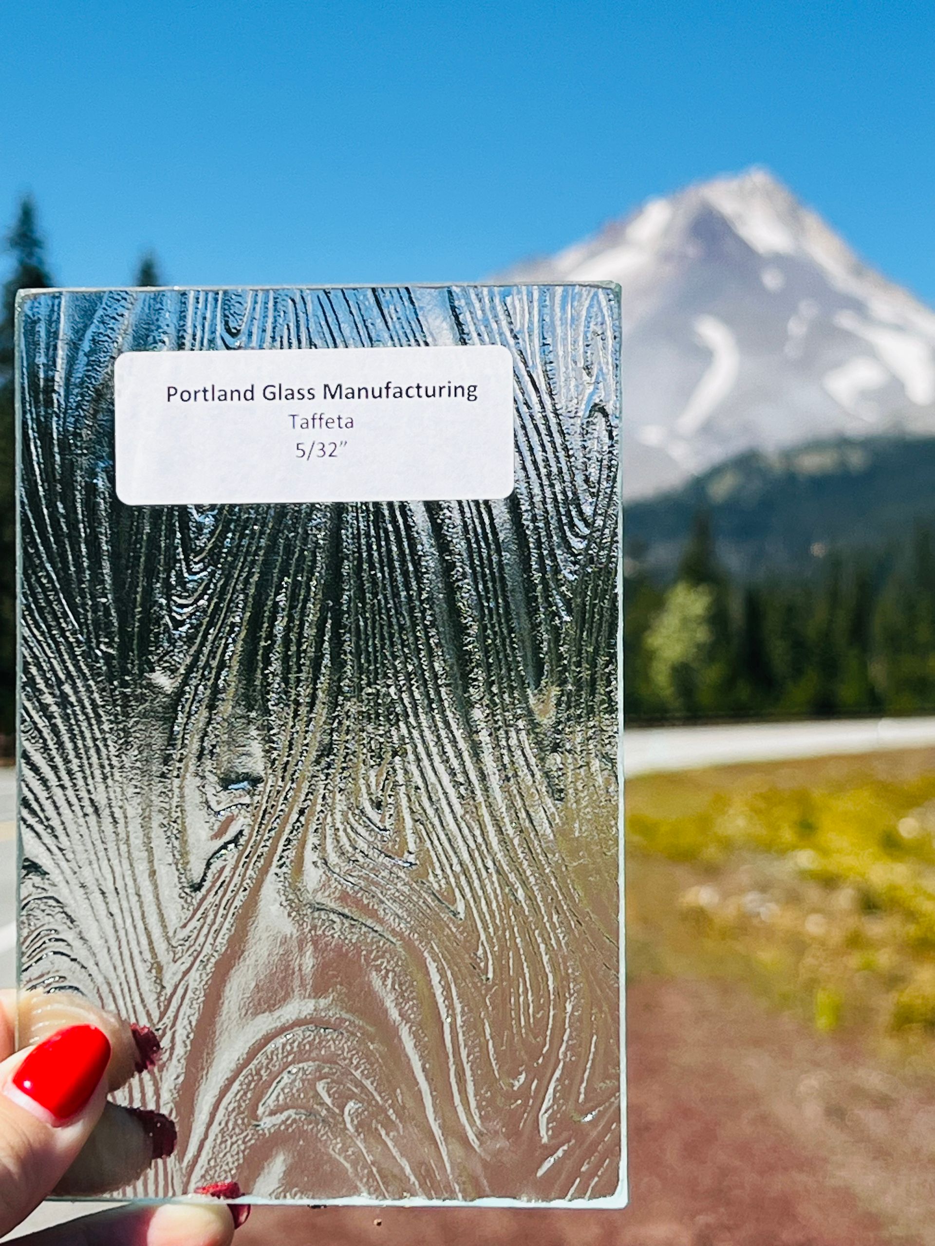 A person holding a piece of glass in front of a mountain