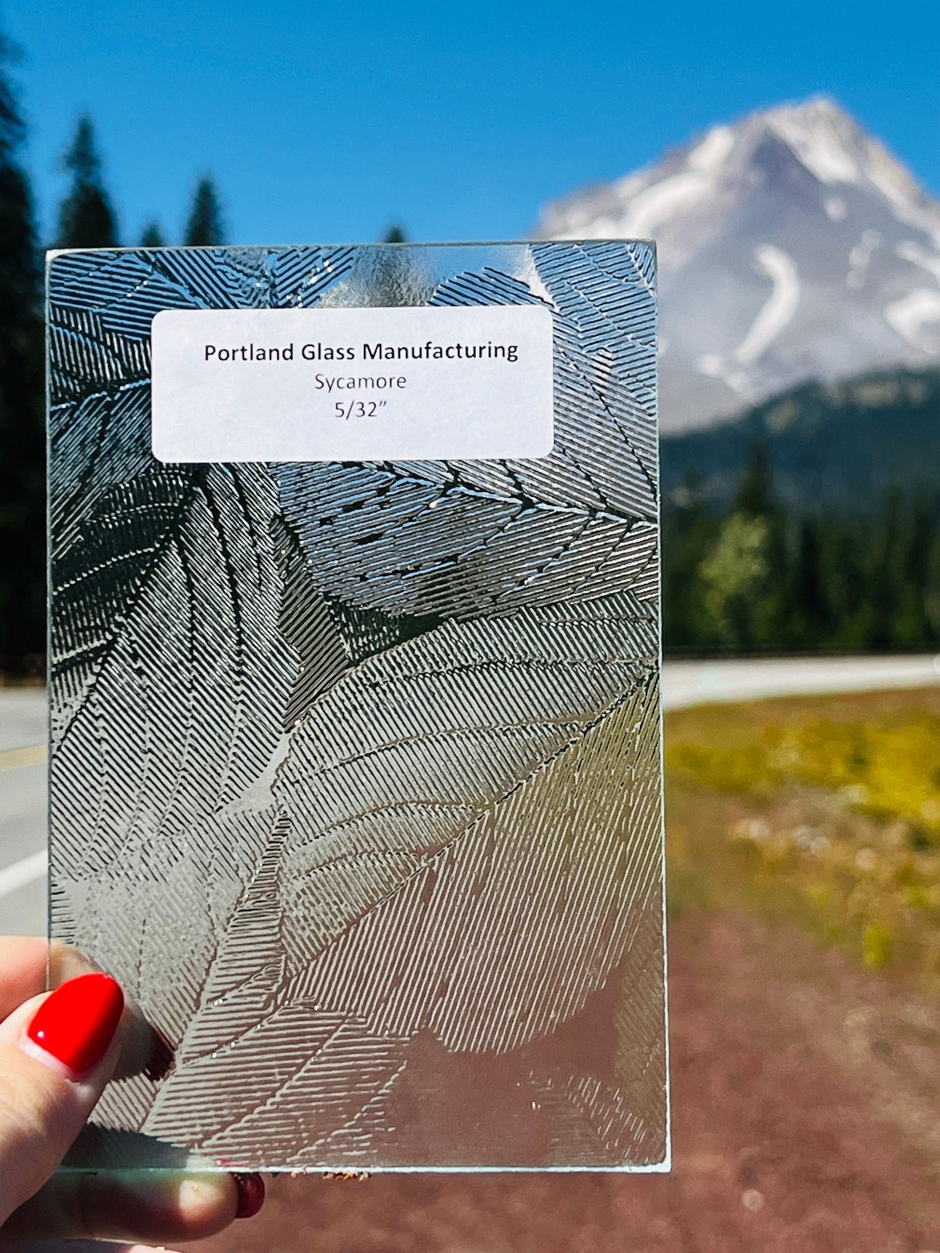 A person is holding a piece of glass in front of a mountain.
