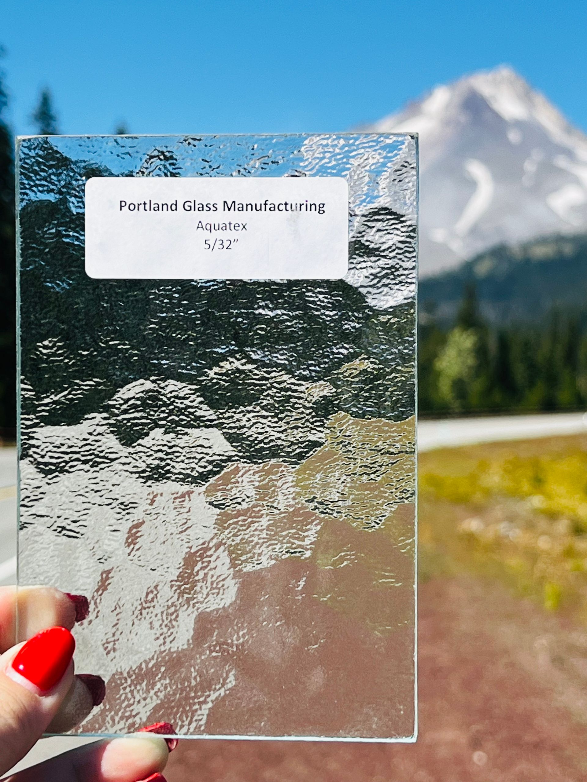 A person is holding a piece of glass with a mountain in the background.