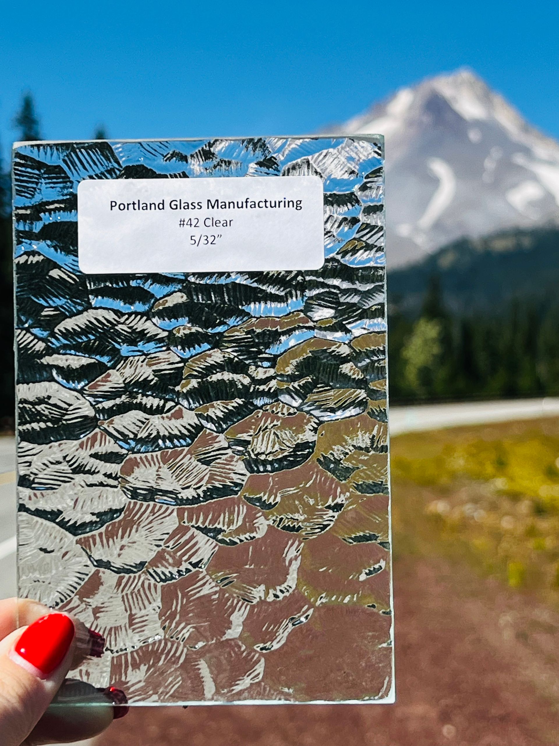 A person holding a piece of glass with a mountain in the background