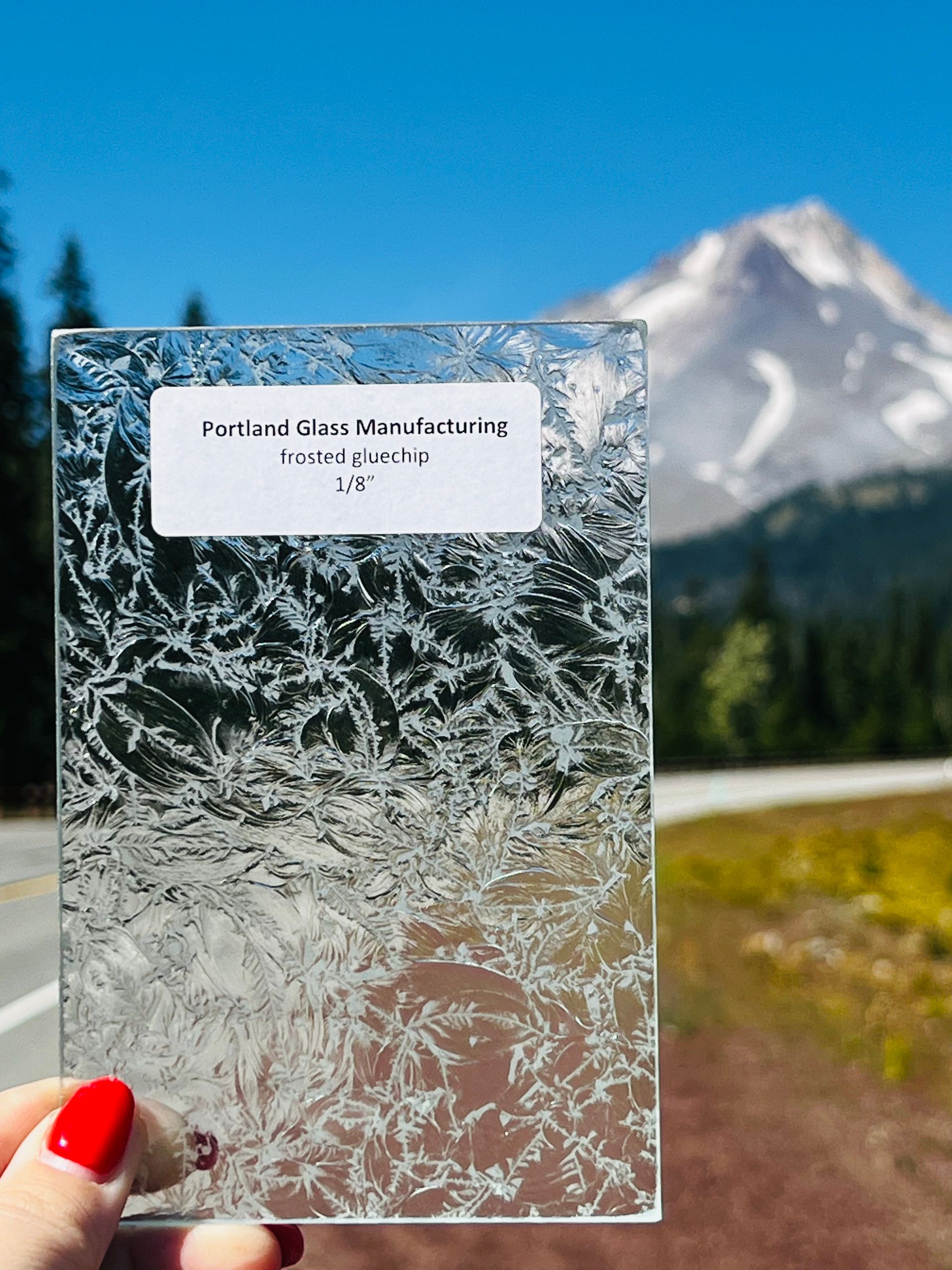 A person is holding a piece of glass in front of a mountain.
