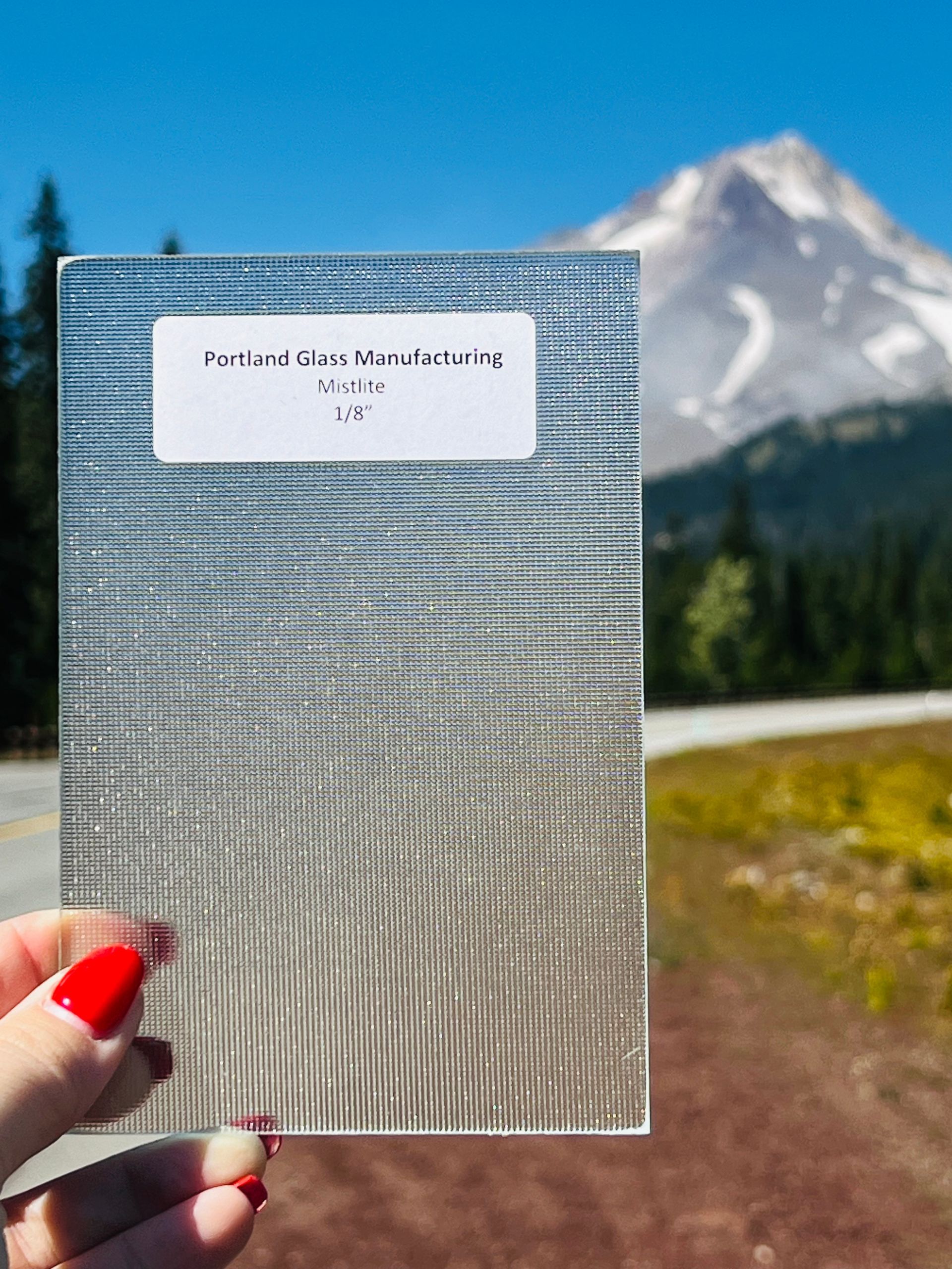 A person holding a piece of glass with a mountain in the background