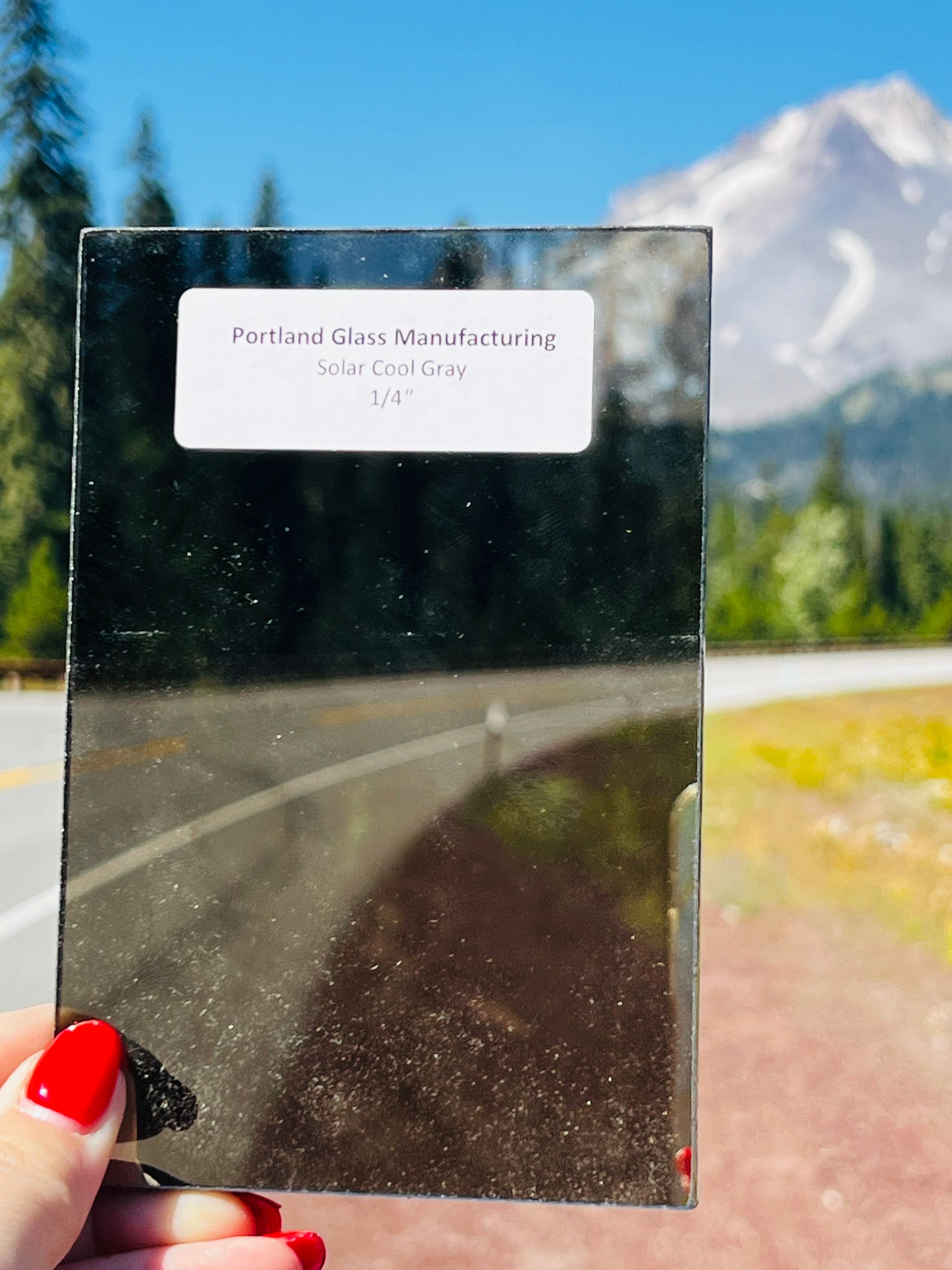 A person is holding a piece of glass in front of a mountain.