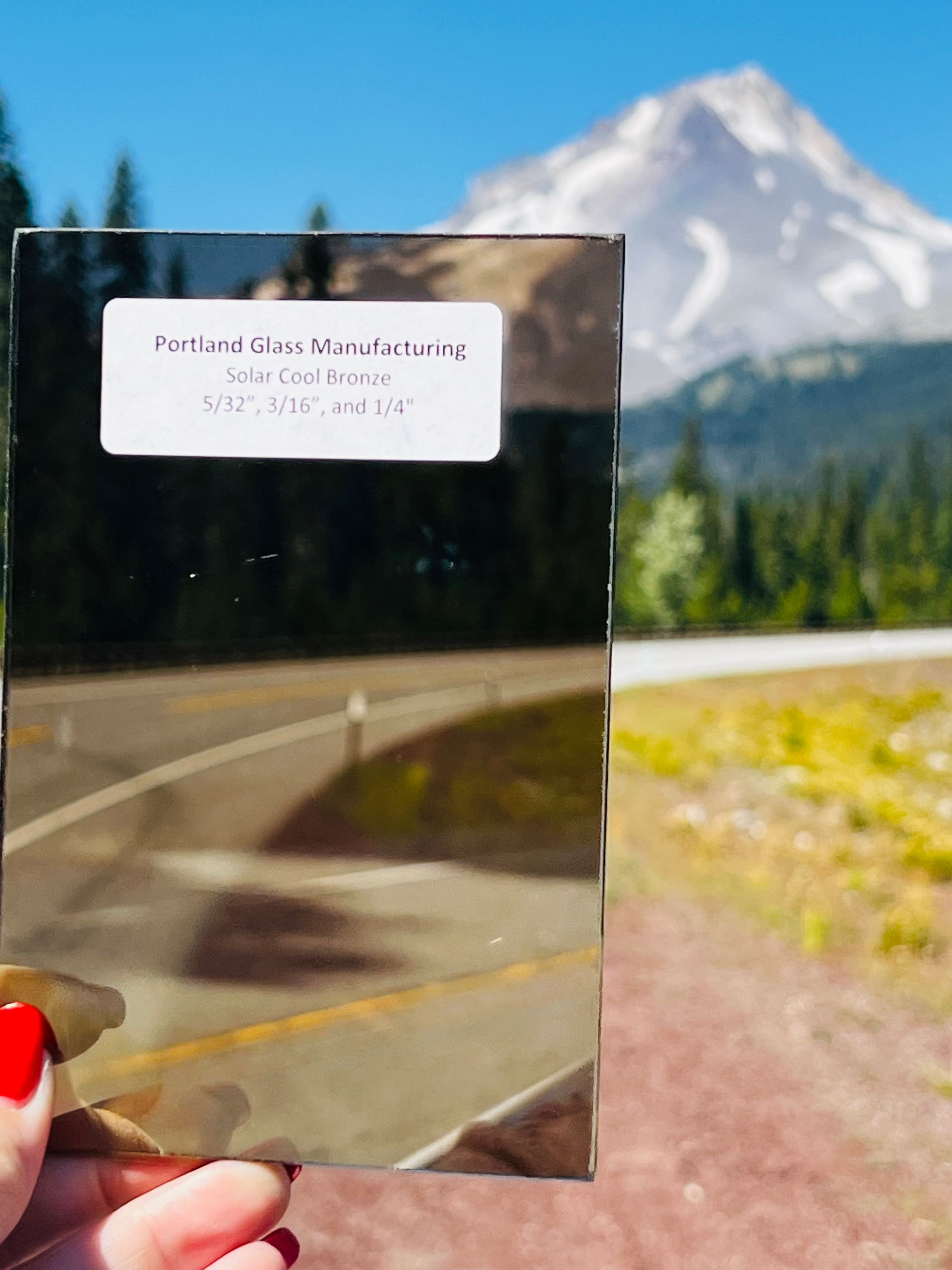 A person holding a piece of glass with a mountain in the background