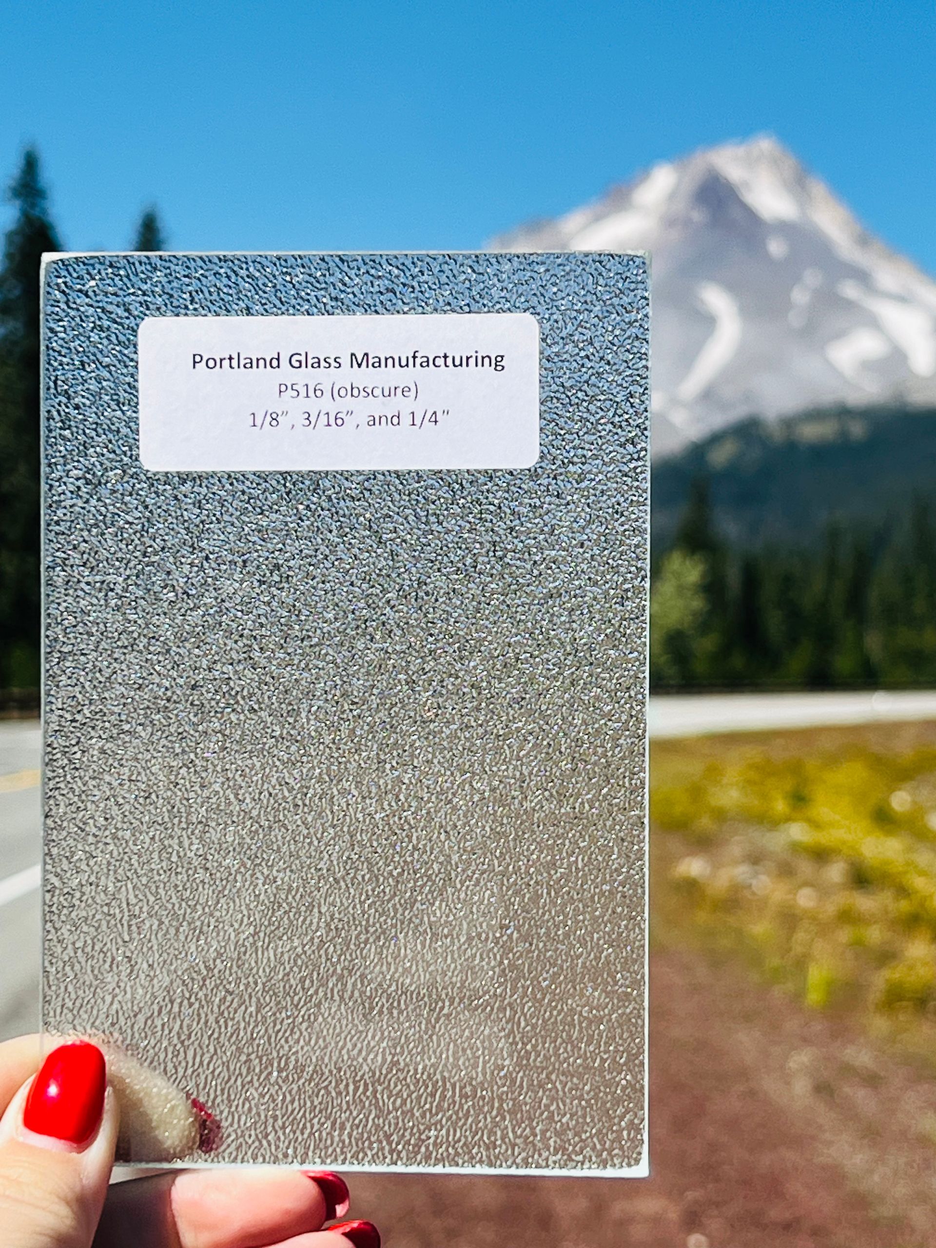 A person is holding a piece of glass in front of a mountain.