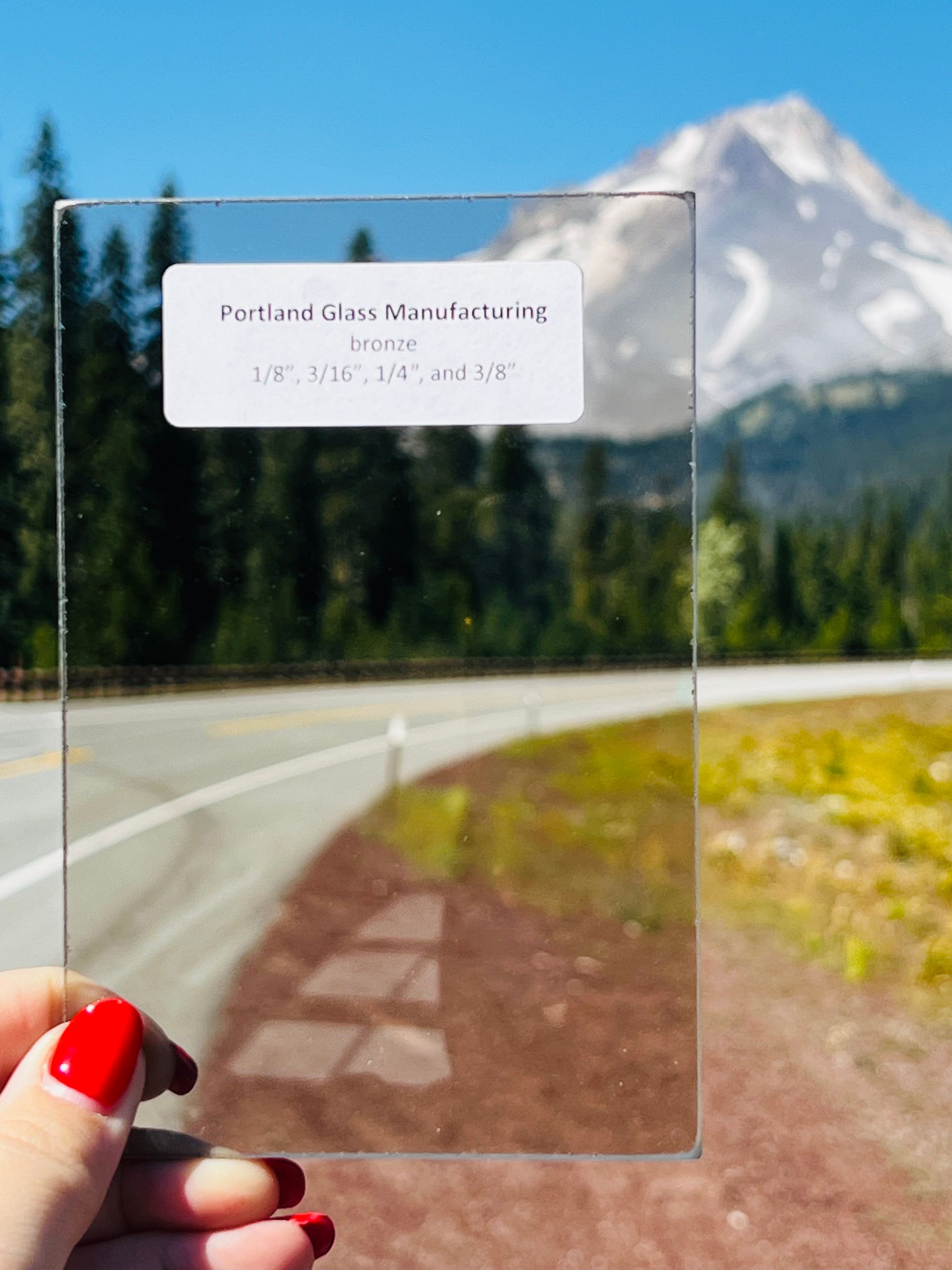 A person holding a piece of glass with a mountain in the background