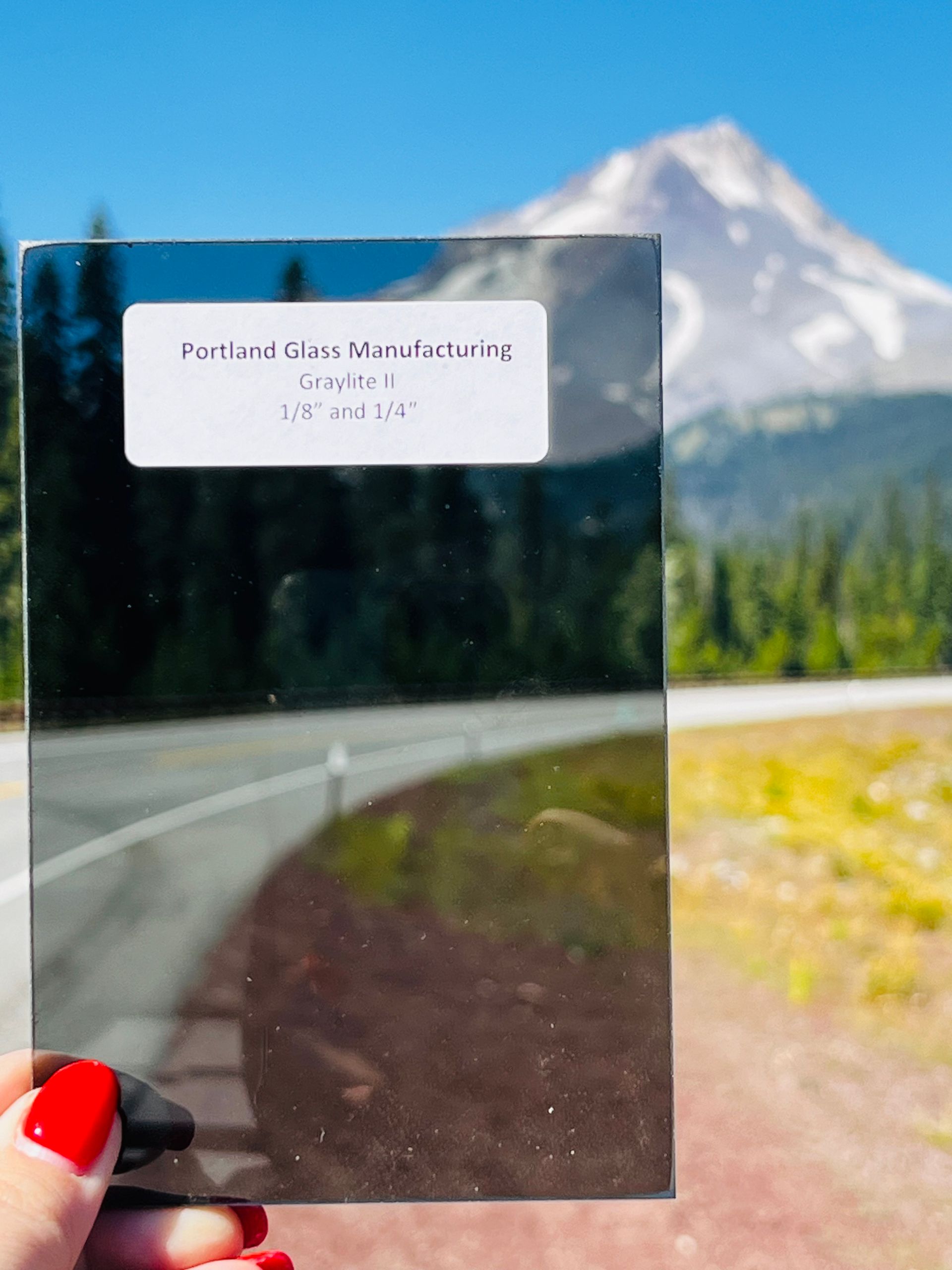 A person holding a piece of glass with a mountain in the background