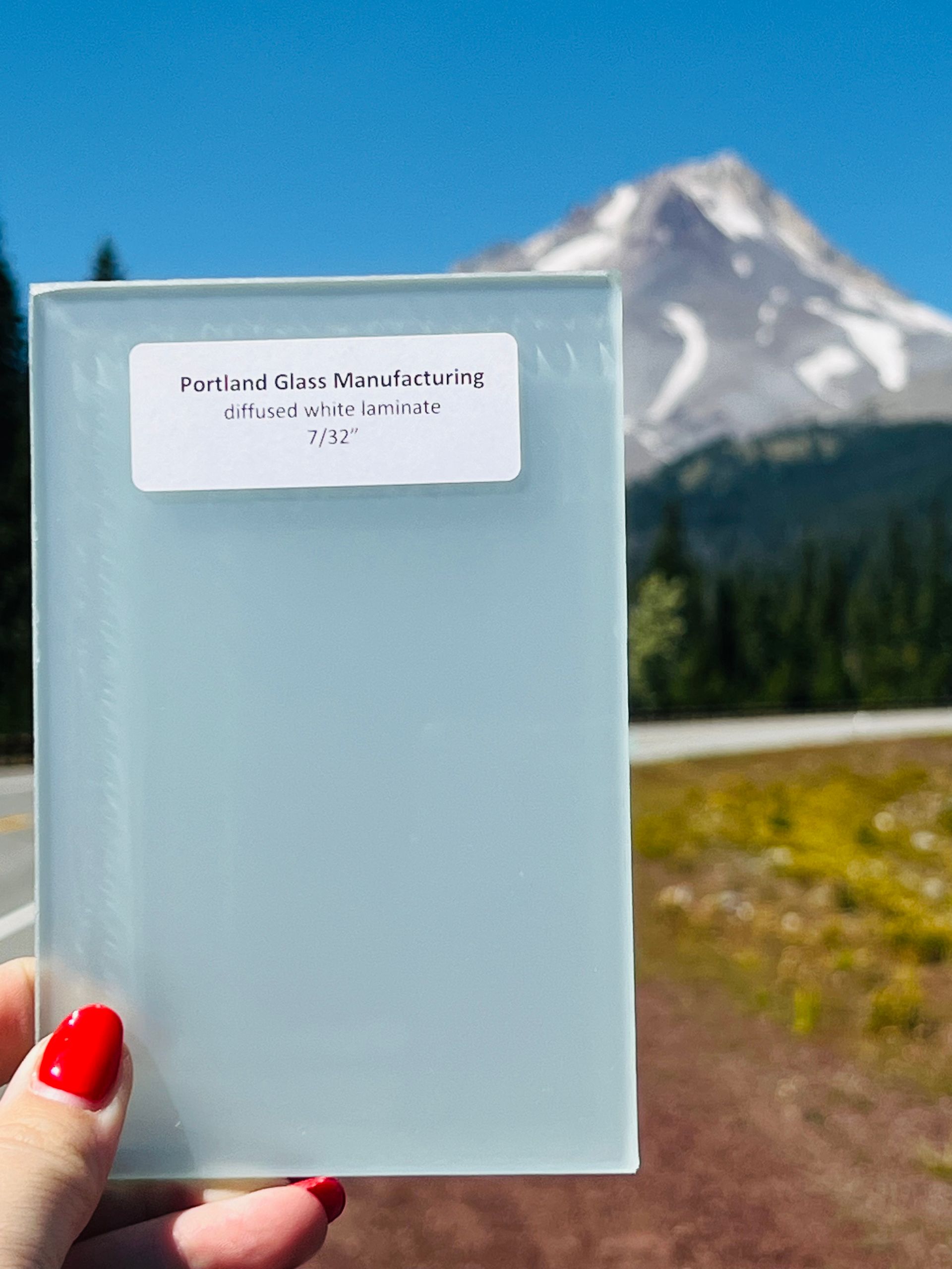 A person holding a piece of glass with a mountain in the background