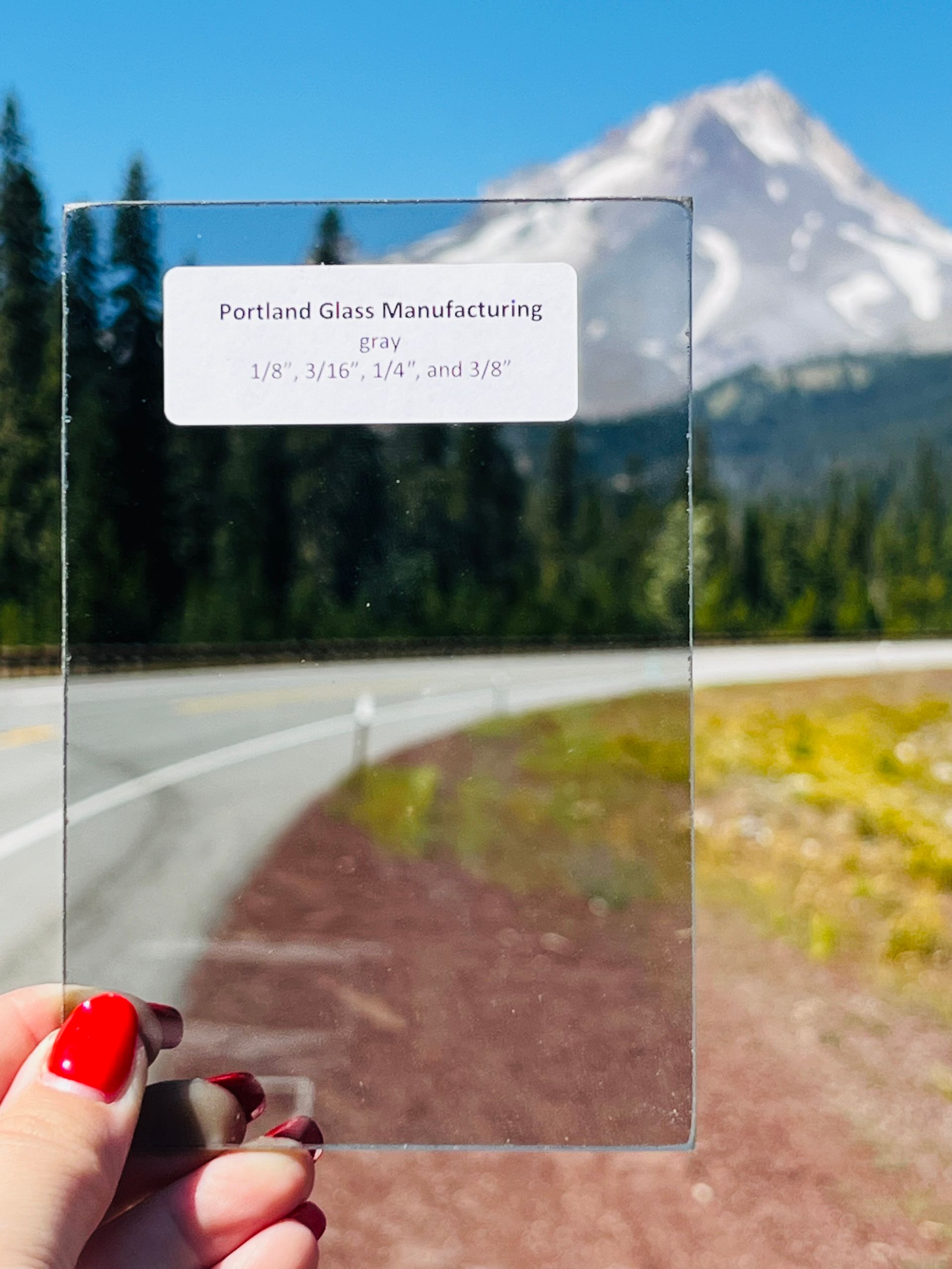 A person is holding a piece of glass in front of a mountain.