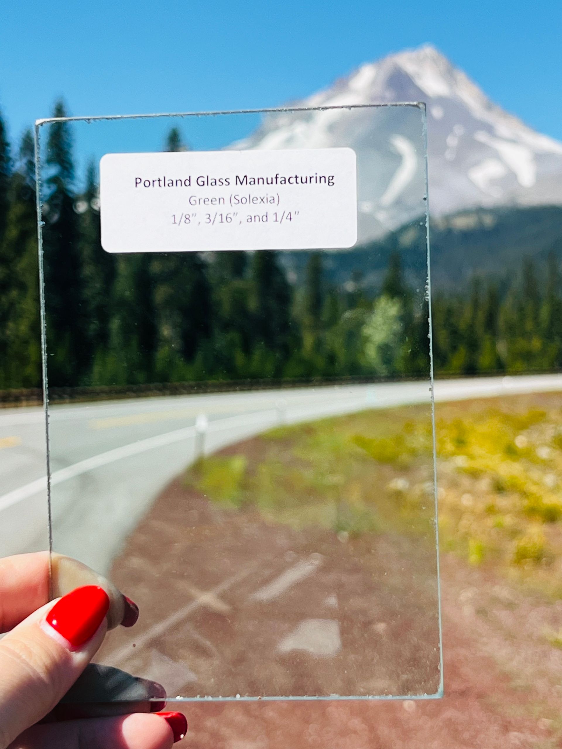 A person holding a piece of glass in front of a mountain