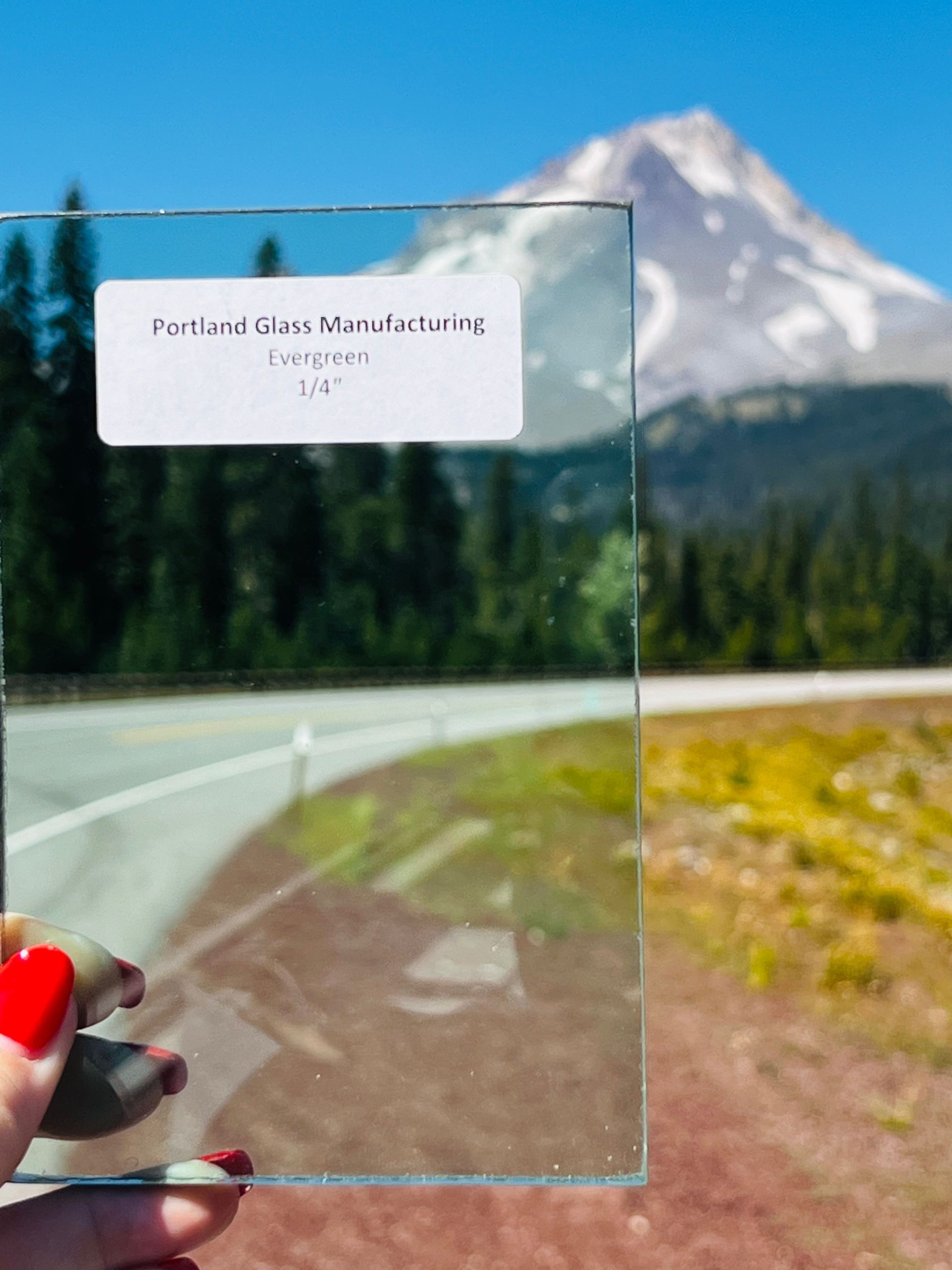 A person is holding a piece of glass in front of a mountain.