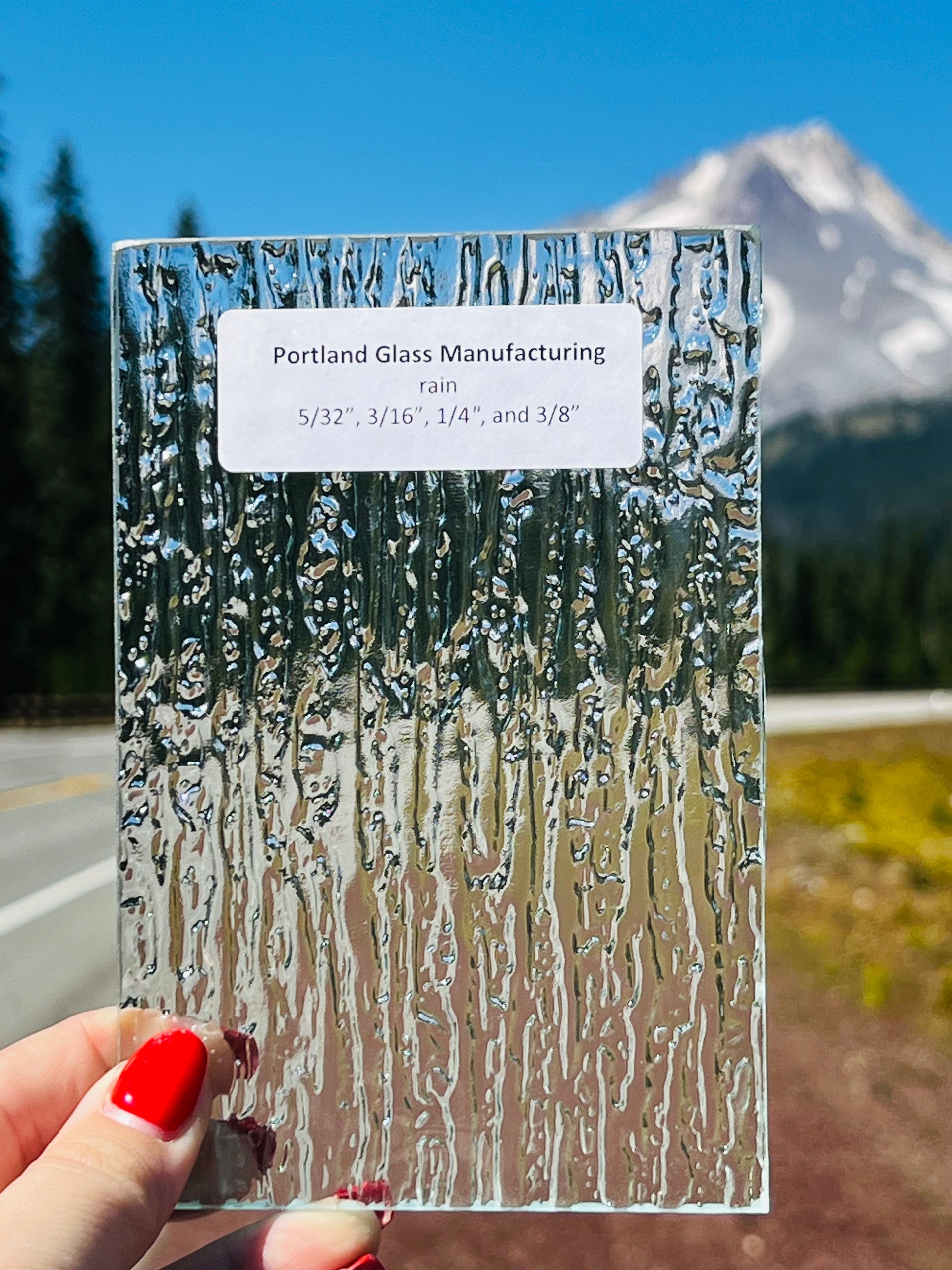 A person holding a piece of glass with a mountain in the background