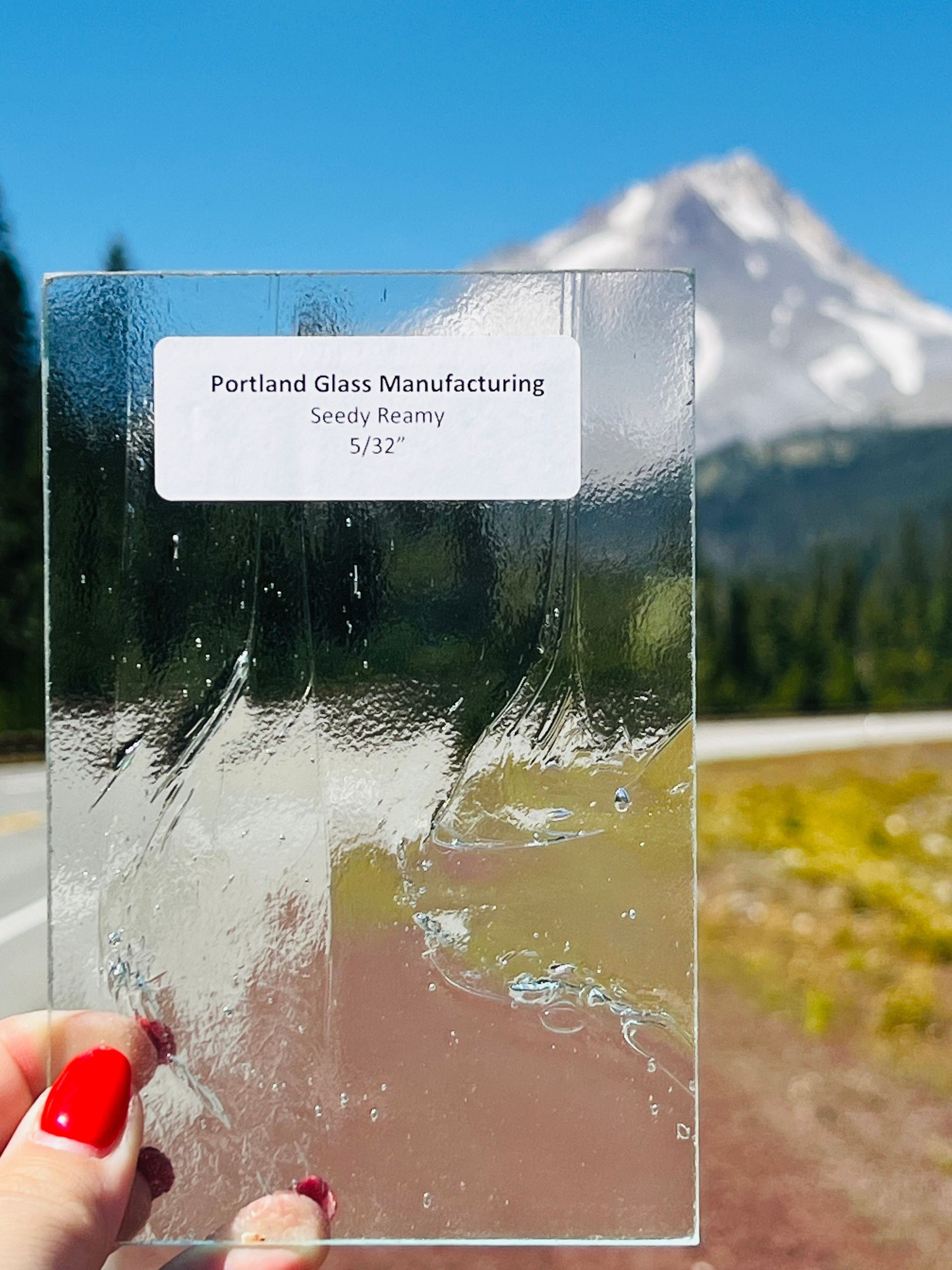 A person is holding a piece of glass in front of a mountain.