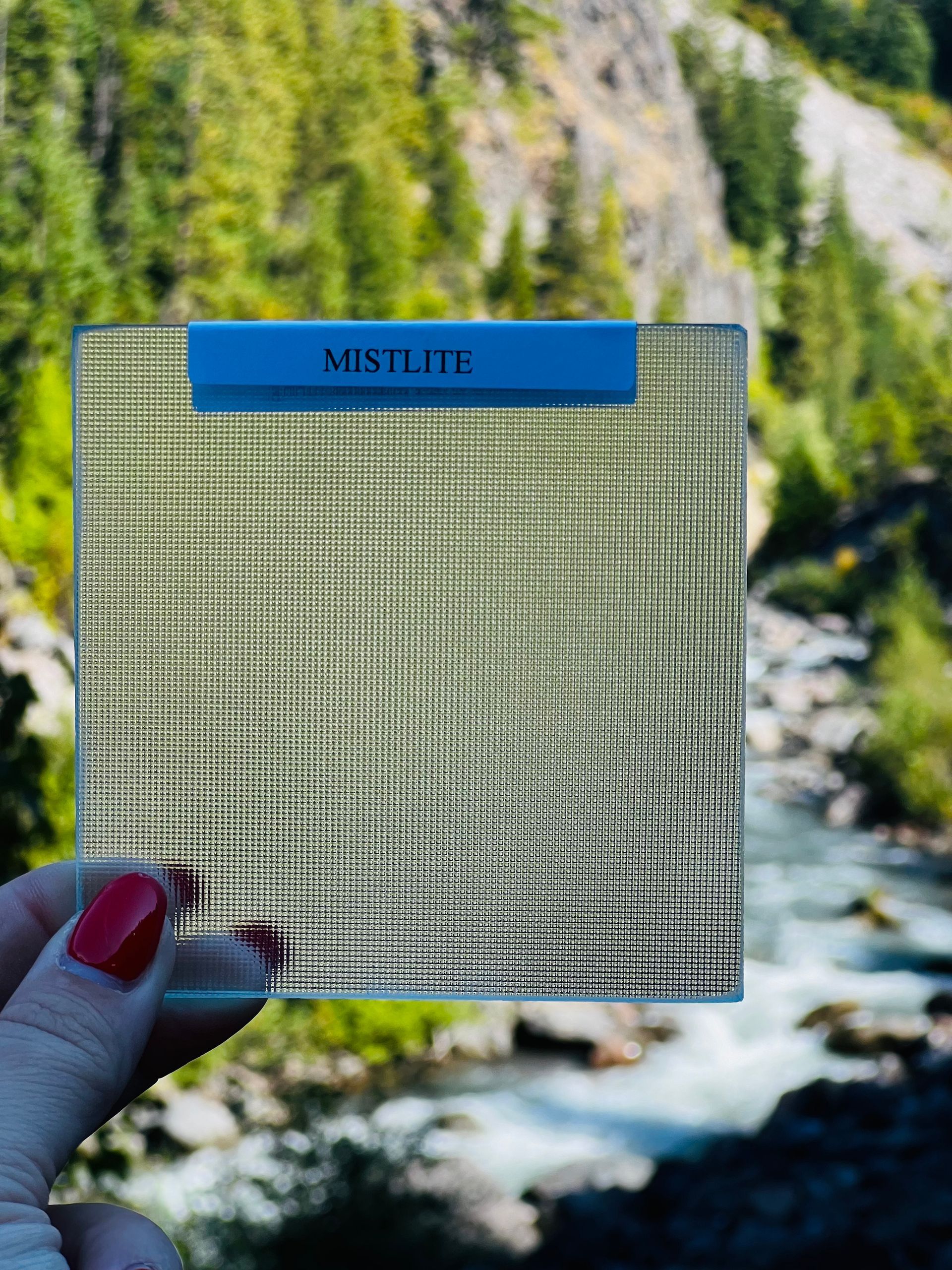 A person is holding a piece of glass in front of a river.