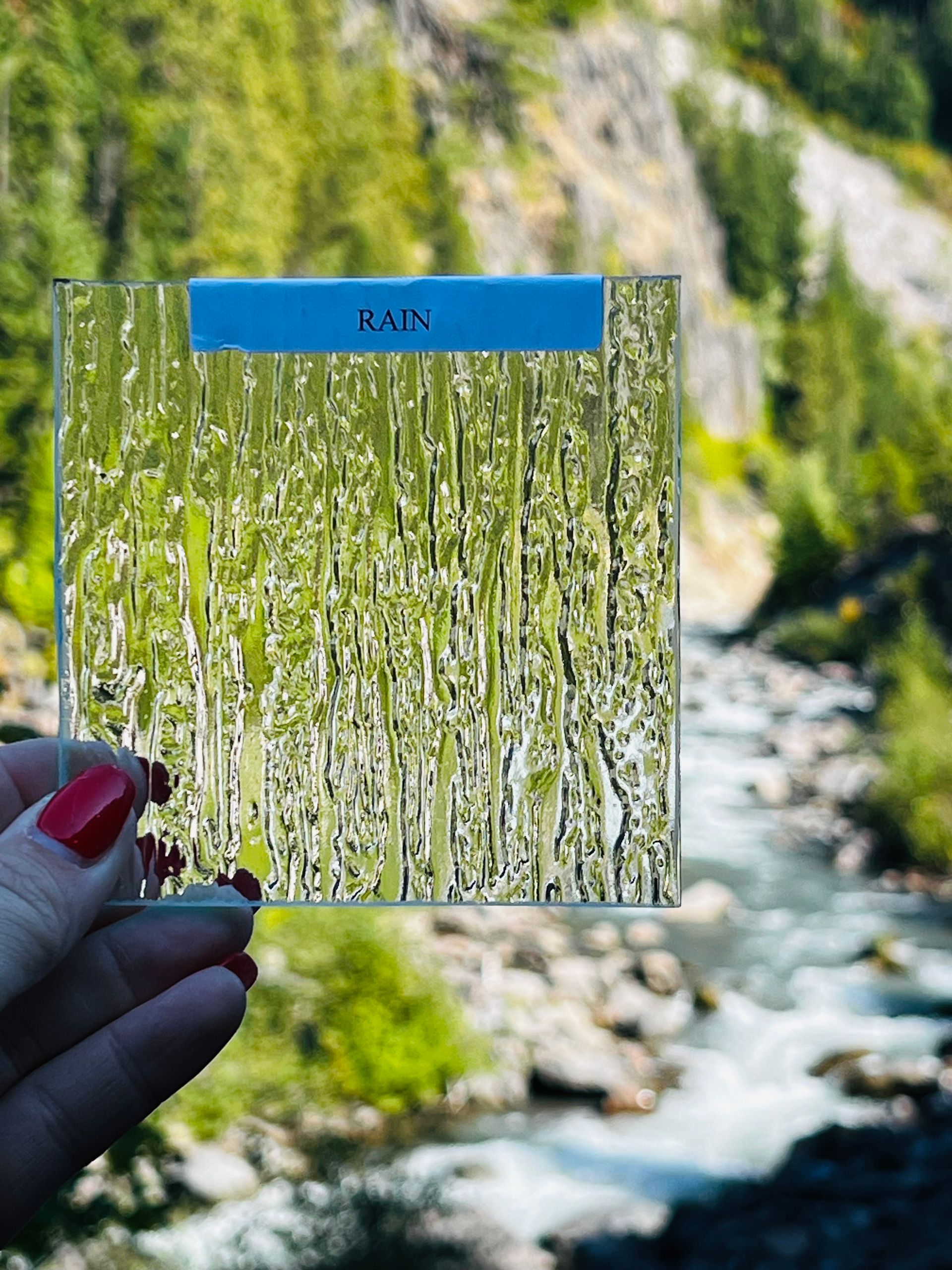 A person is holding a piece of glass in front of a river.