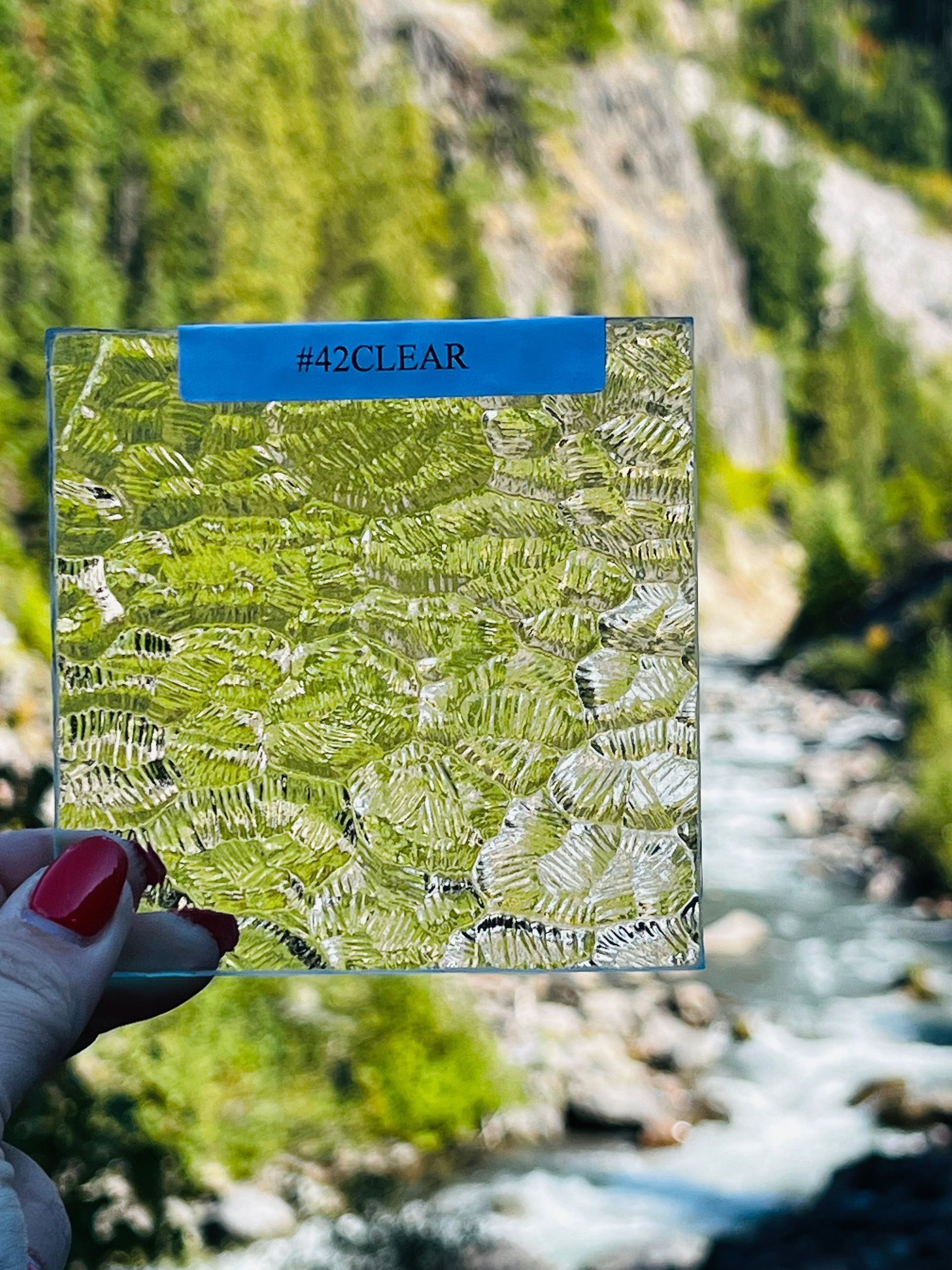 A woman is holding a piece of glass in front of a river.