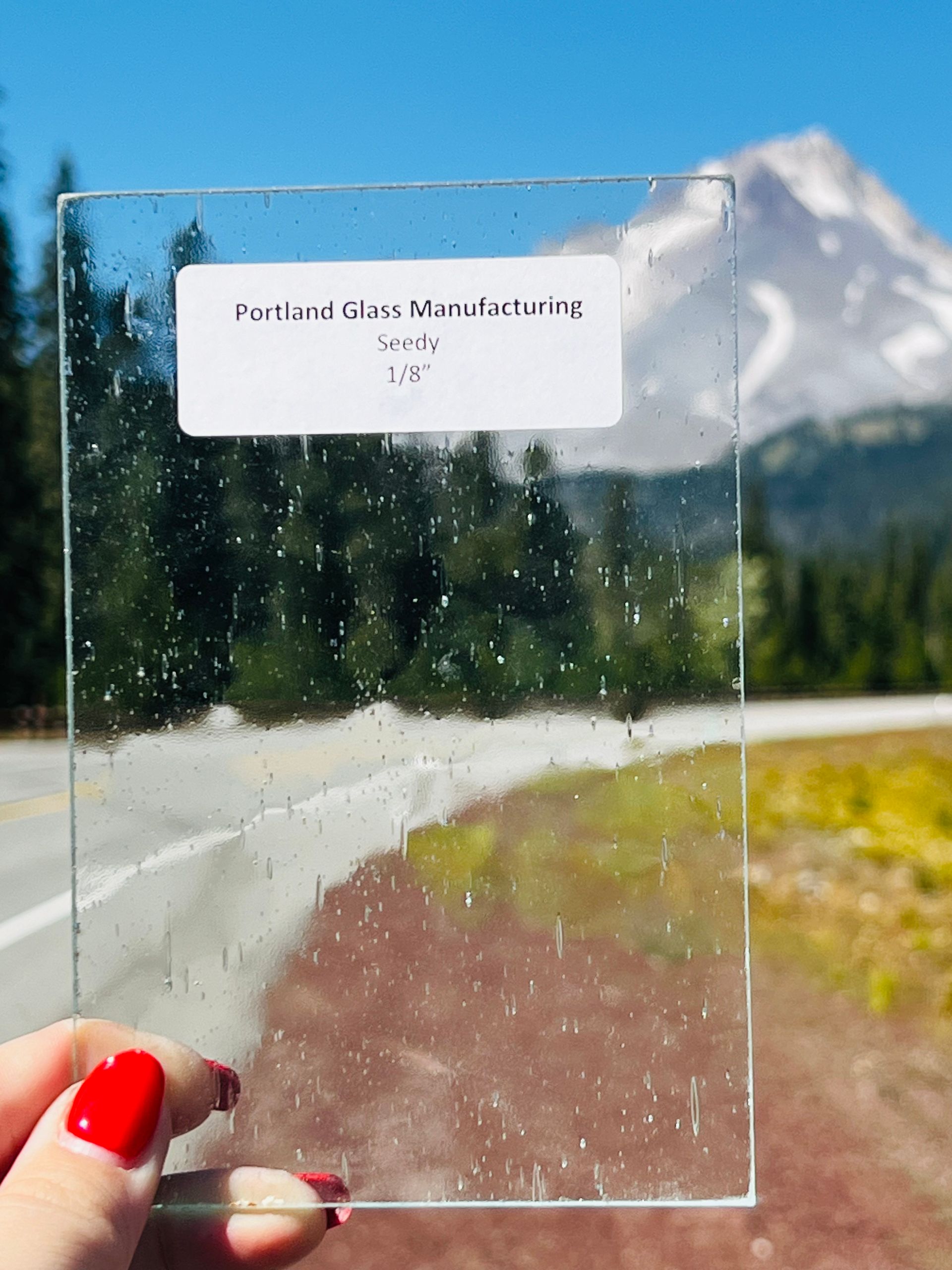 A person is holding a piece of glass in front of a mountain.