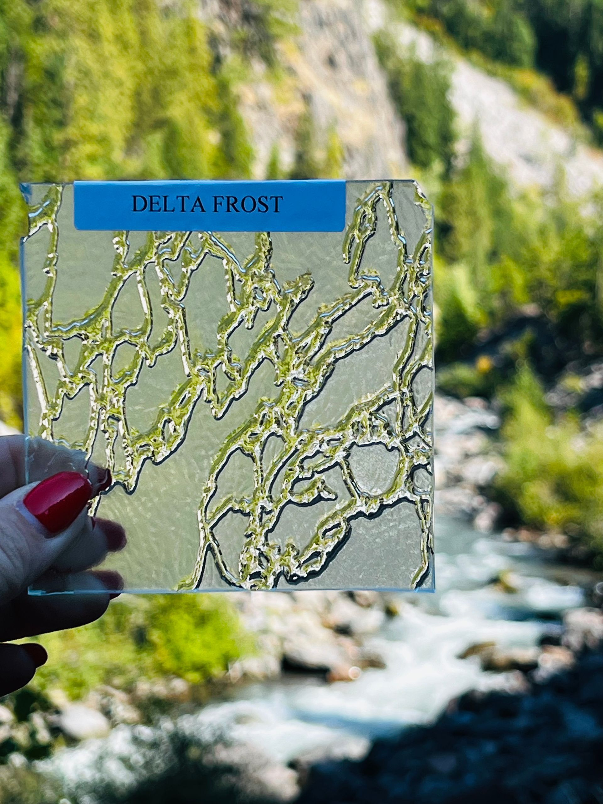 A woman is holding a piece of glass in front of a river.