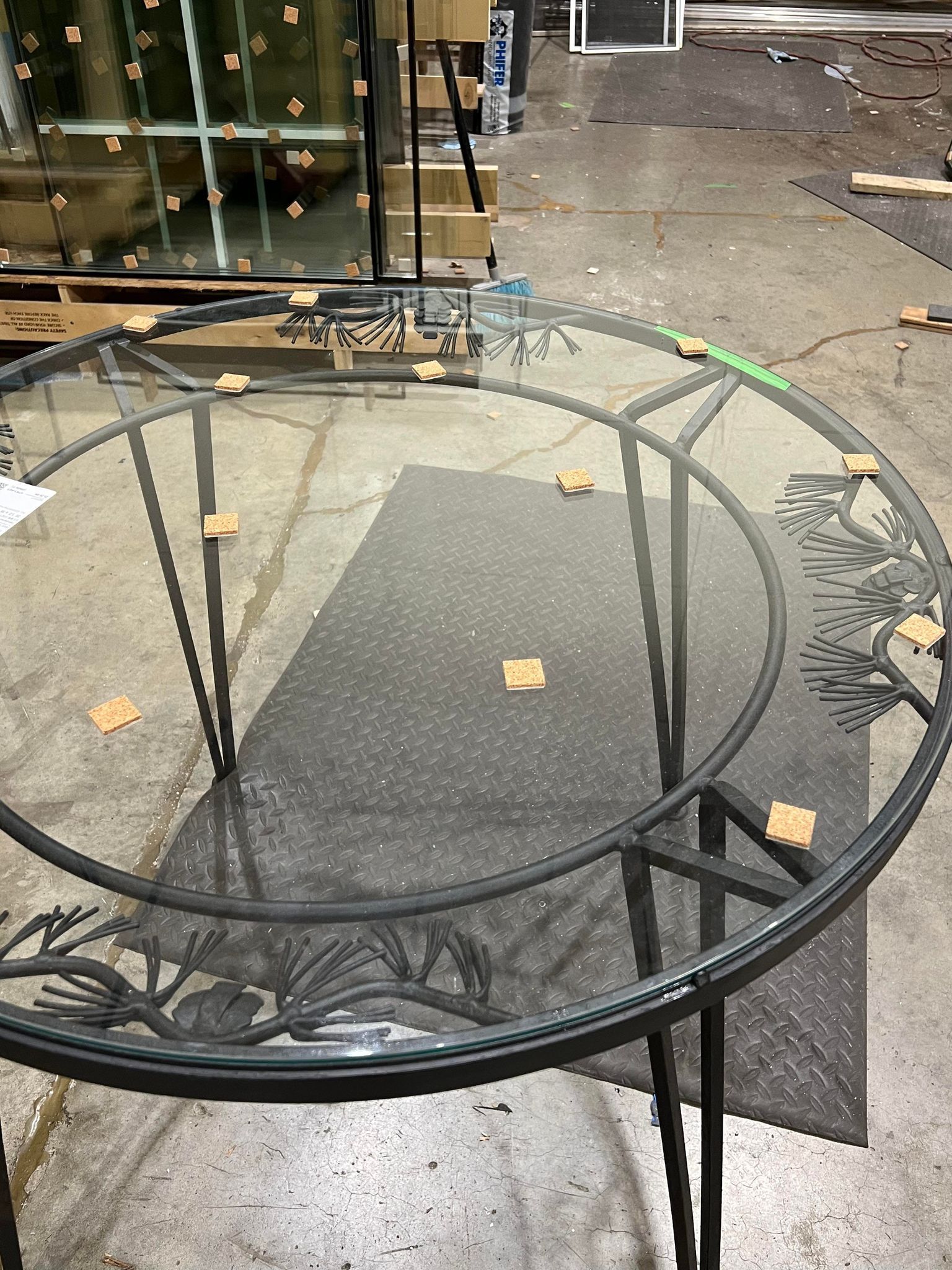 A round glass table with a black frame is sitting on a concrete floor in a warehouse.