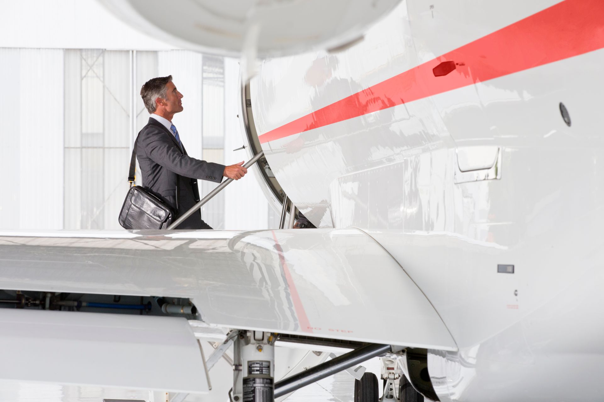 Man in suit opening airplane door on tarmac.