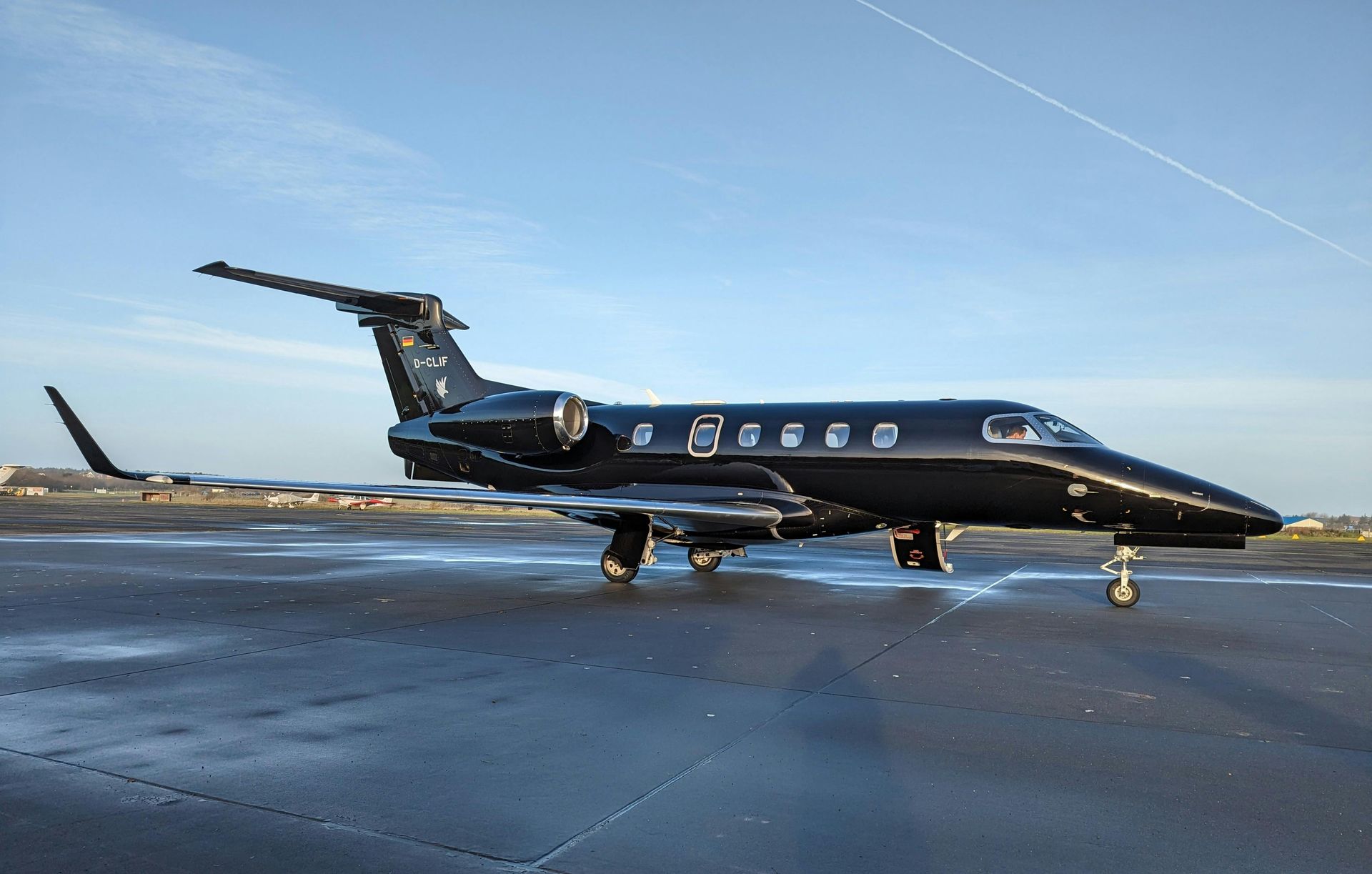 Black private jet on an airport tarmac under a blue sky, with wing tip details visible.