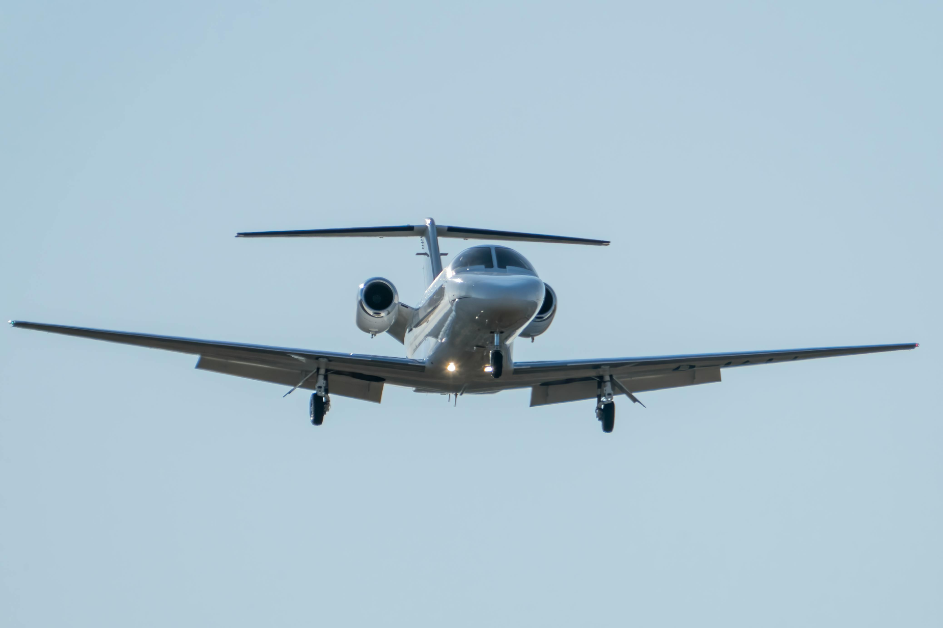 A silver jet airplane in flight, viewed head-on against a clear sky.