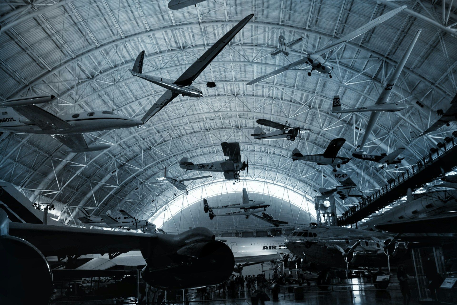 Aircraft hang in a large, arched hall; examples include biplanes and gliders.