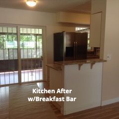 A kitchen area featuring a white breakfast bar with a granite countertop, a dark refrigerator, and a sliding glass door.
