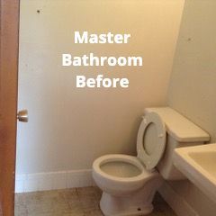 An older, beige-walled master bathroom featuring a white toilet and a portion of a vanity sink.