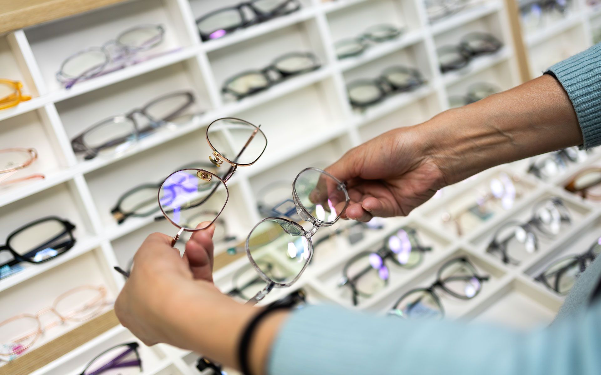 Person holding a pair of eyeglasses in front of a display of other glasses.