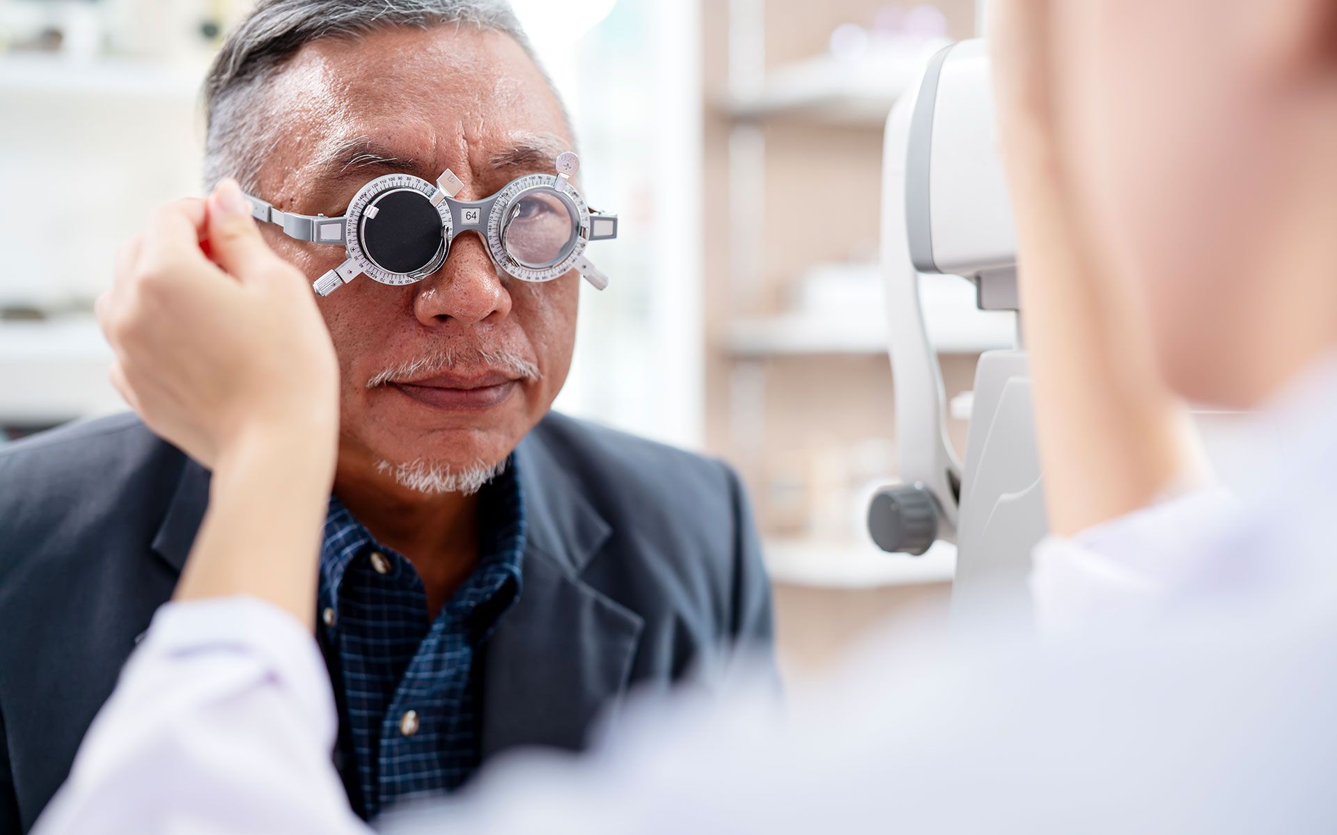 Man wearing eye exam glasses, being examined by a doctor with diagnostic equipment in an office.