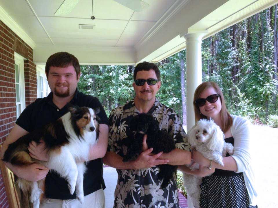 Three people on a porch, each holding a small dog.