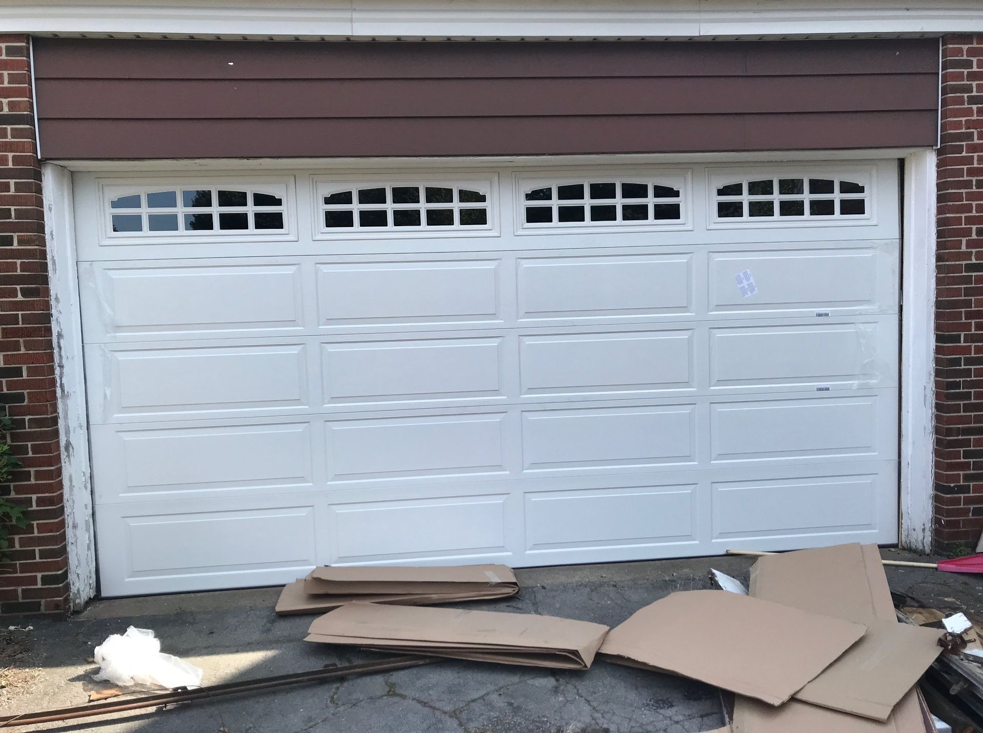 White garage door with rectangular windows, against brick and brown siding. Cardboard boxes on the ground.