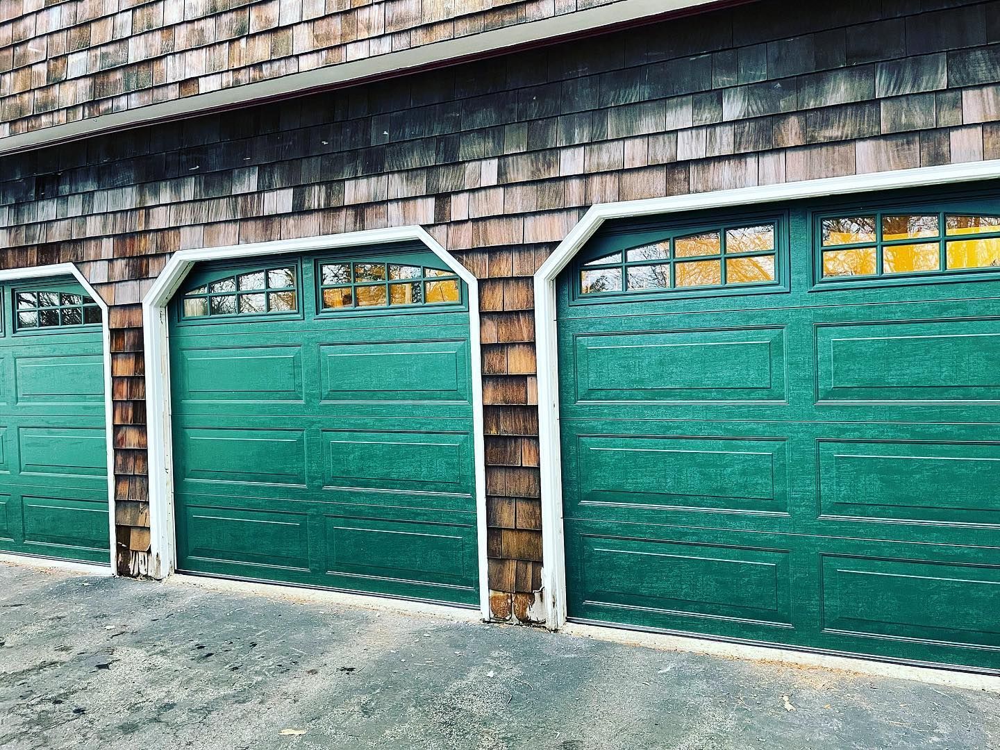 Three green garage doors with glass windows against weathered wooden siding.