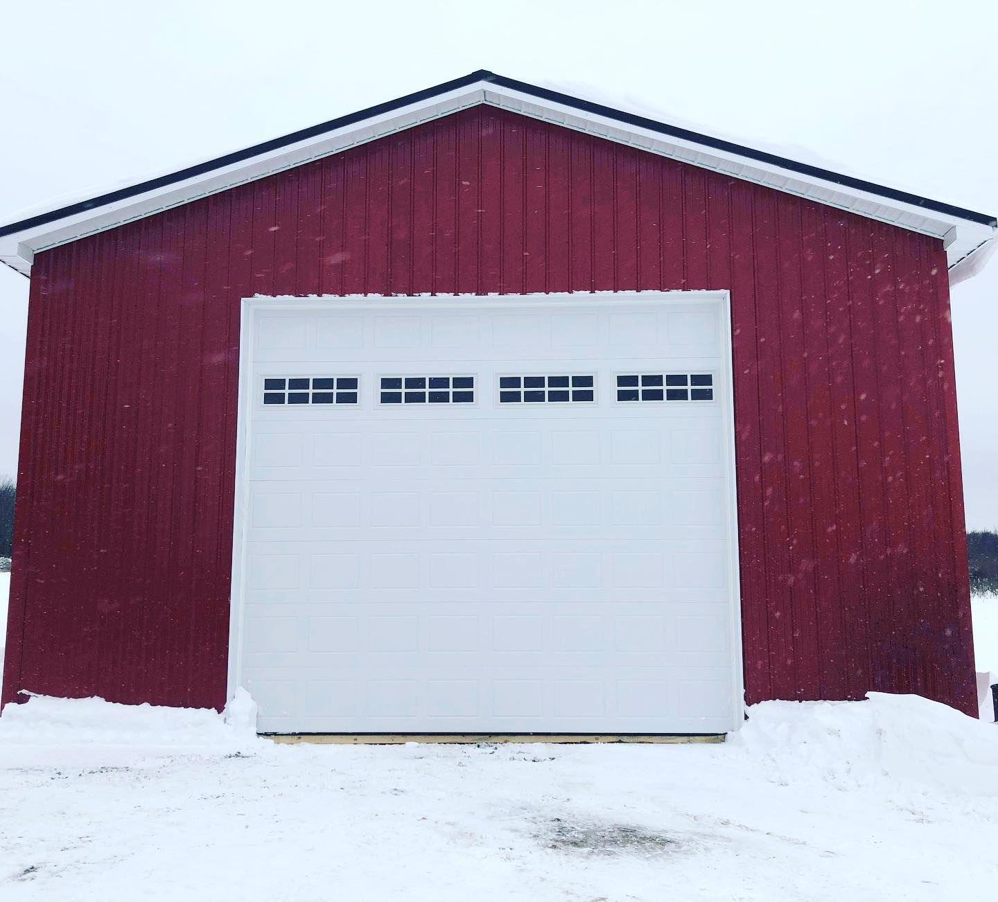 Red barn with white garage door and snow.