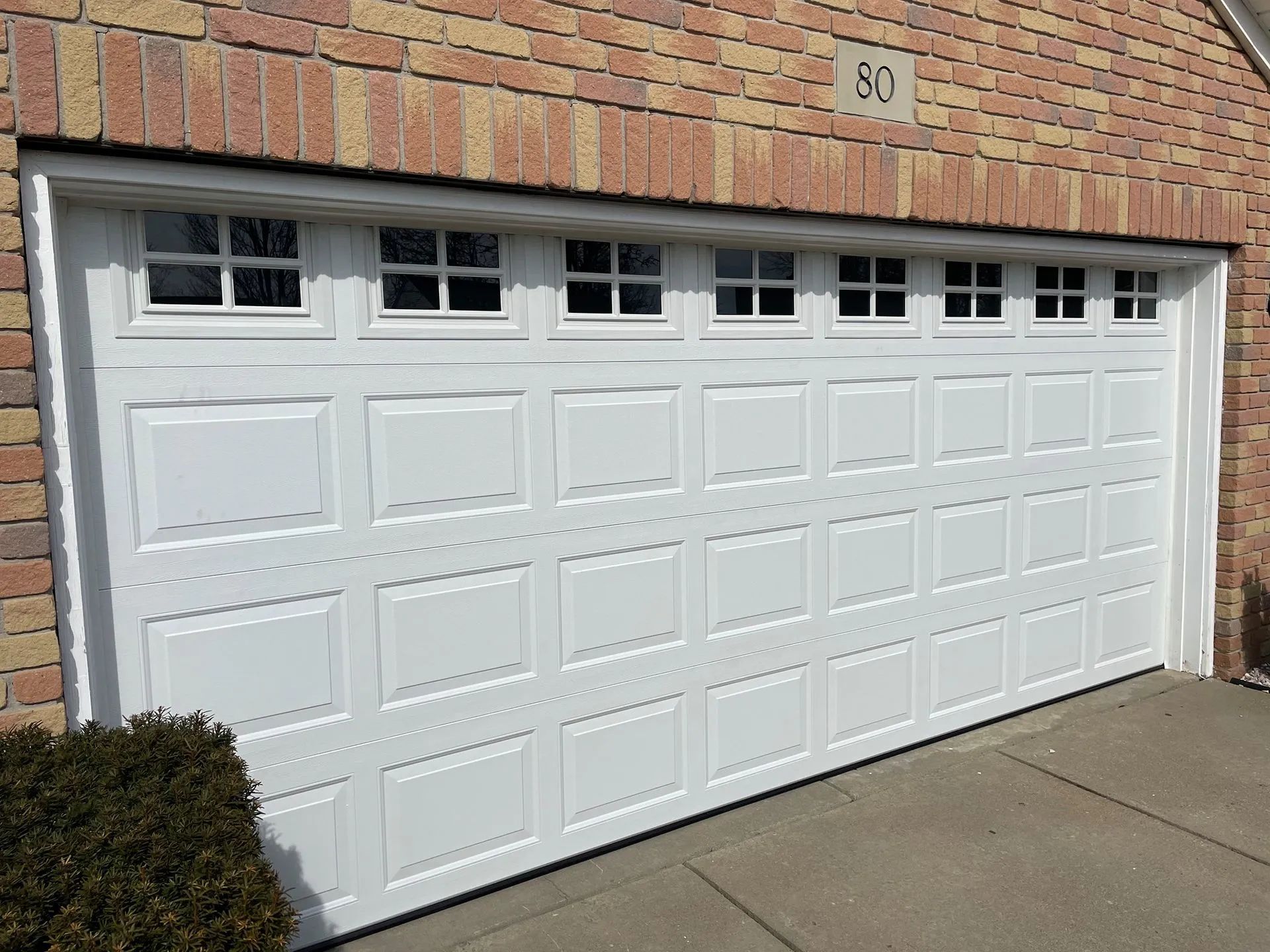 White garage door with small square windows, set in a brick building.