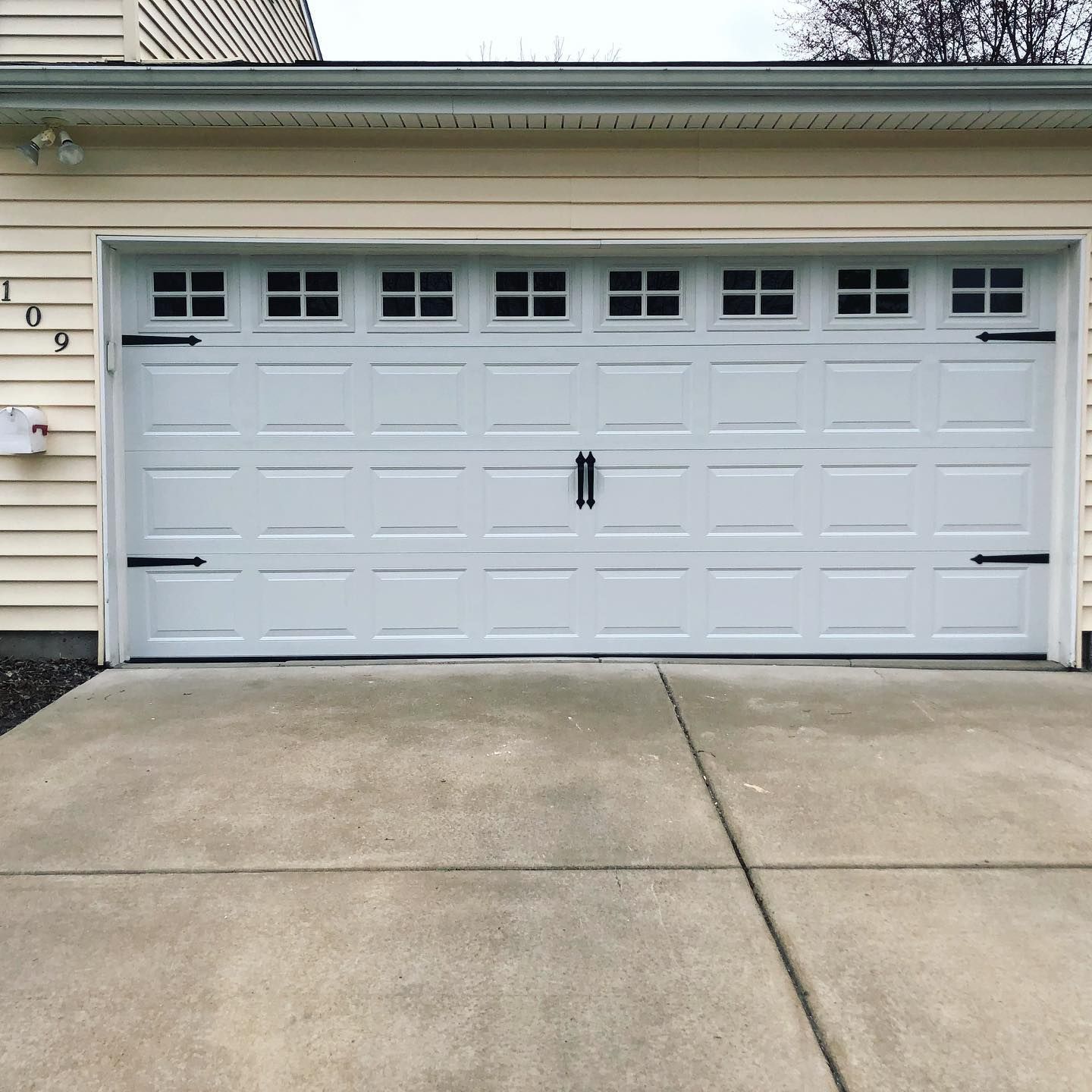 White garage door with decorative hardware, above a concrete driveway.