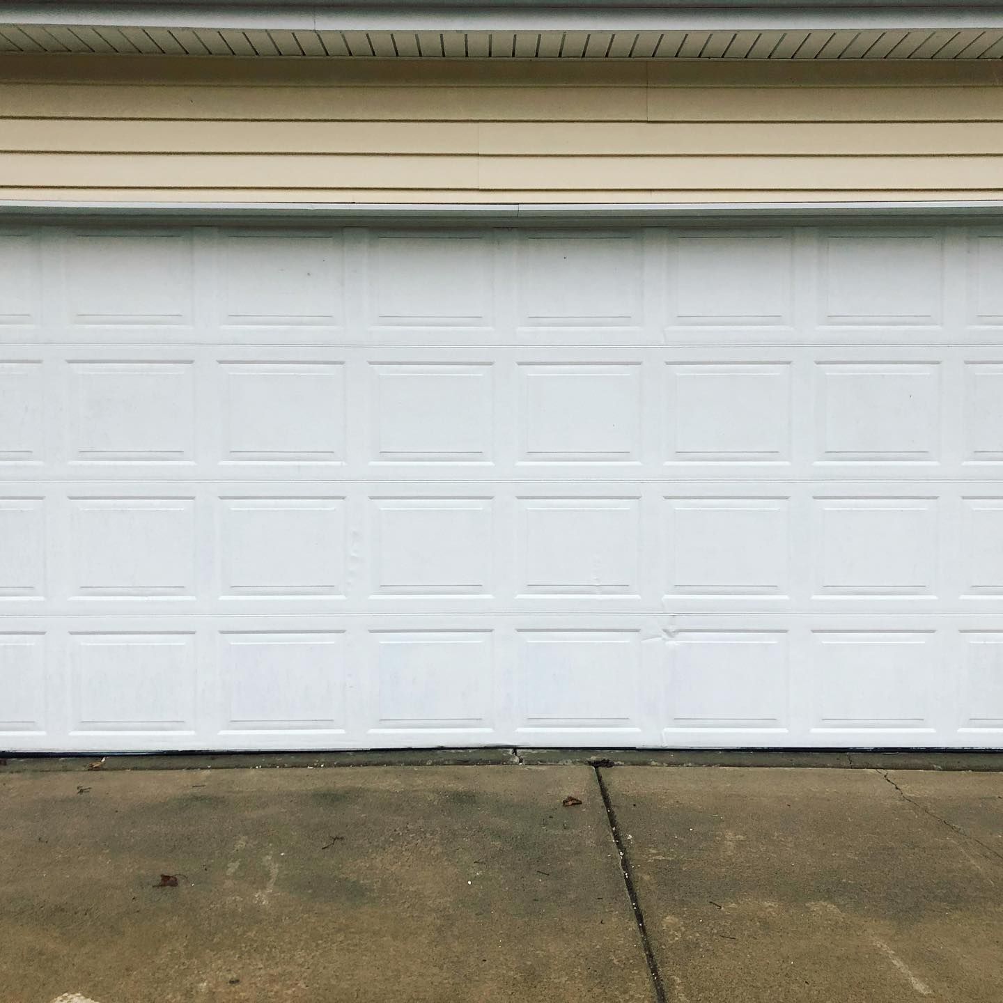 White garage door on a concrete driveway under tan siding.