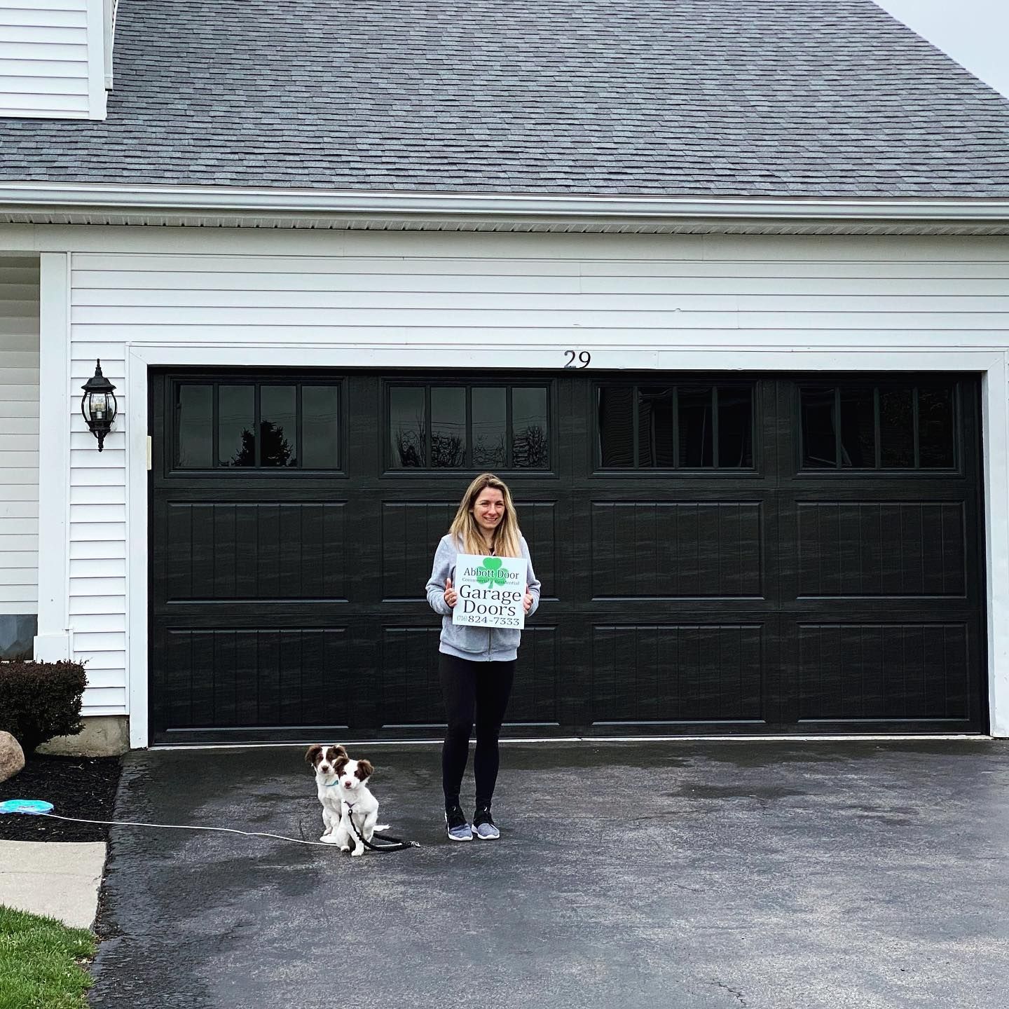 Woman with a dog in front of a black garage door, holding a sign.