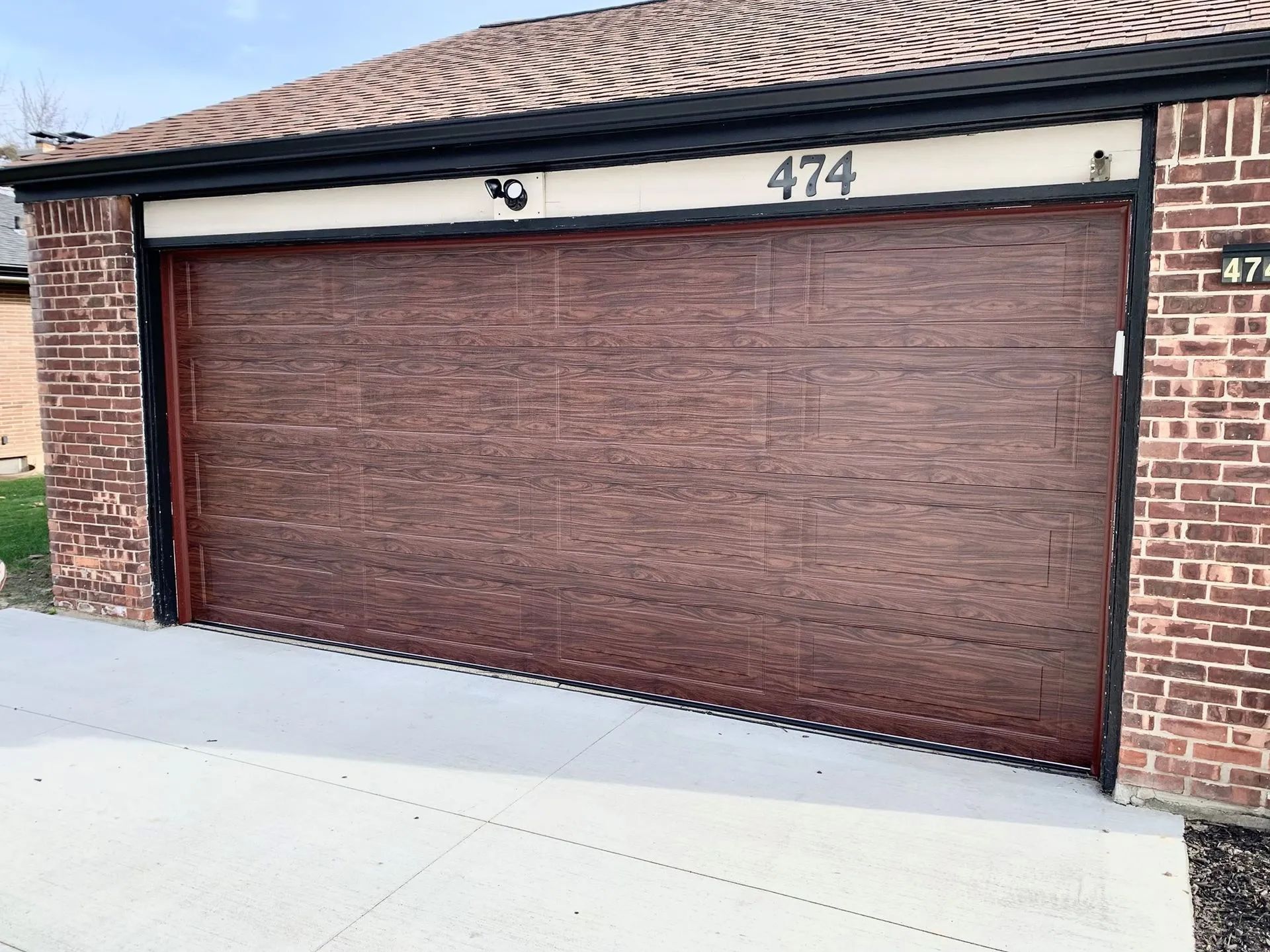 Wooden garage door with windows at top and black hardware, beside a brick wall.