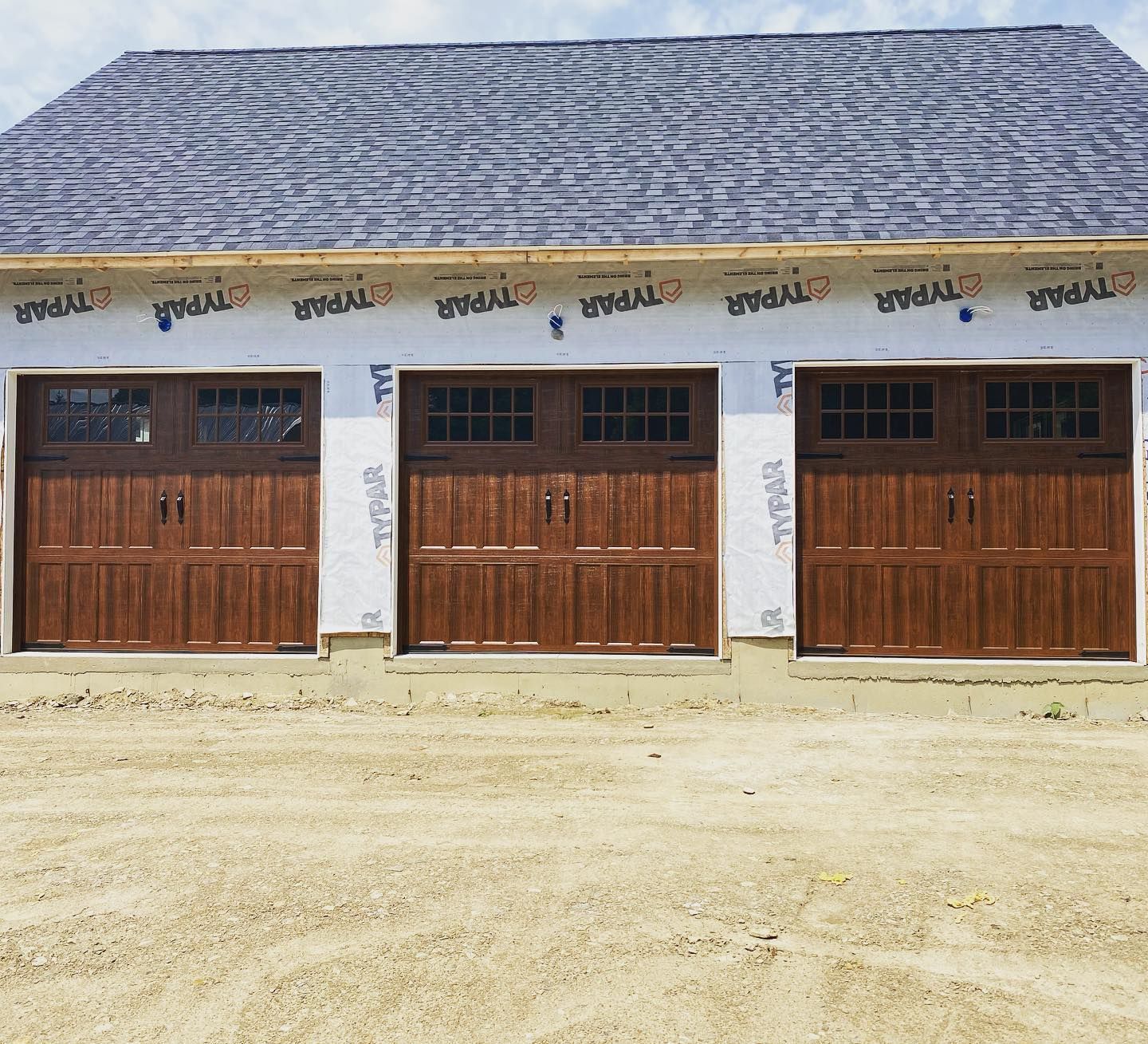 Three brown garage doors with windows beneath a gray roof.