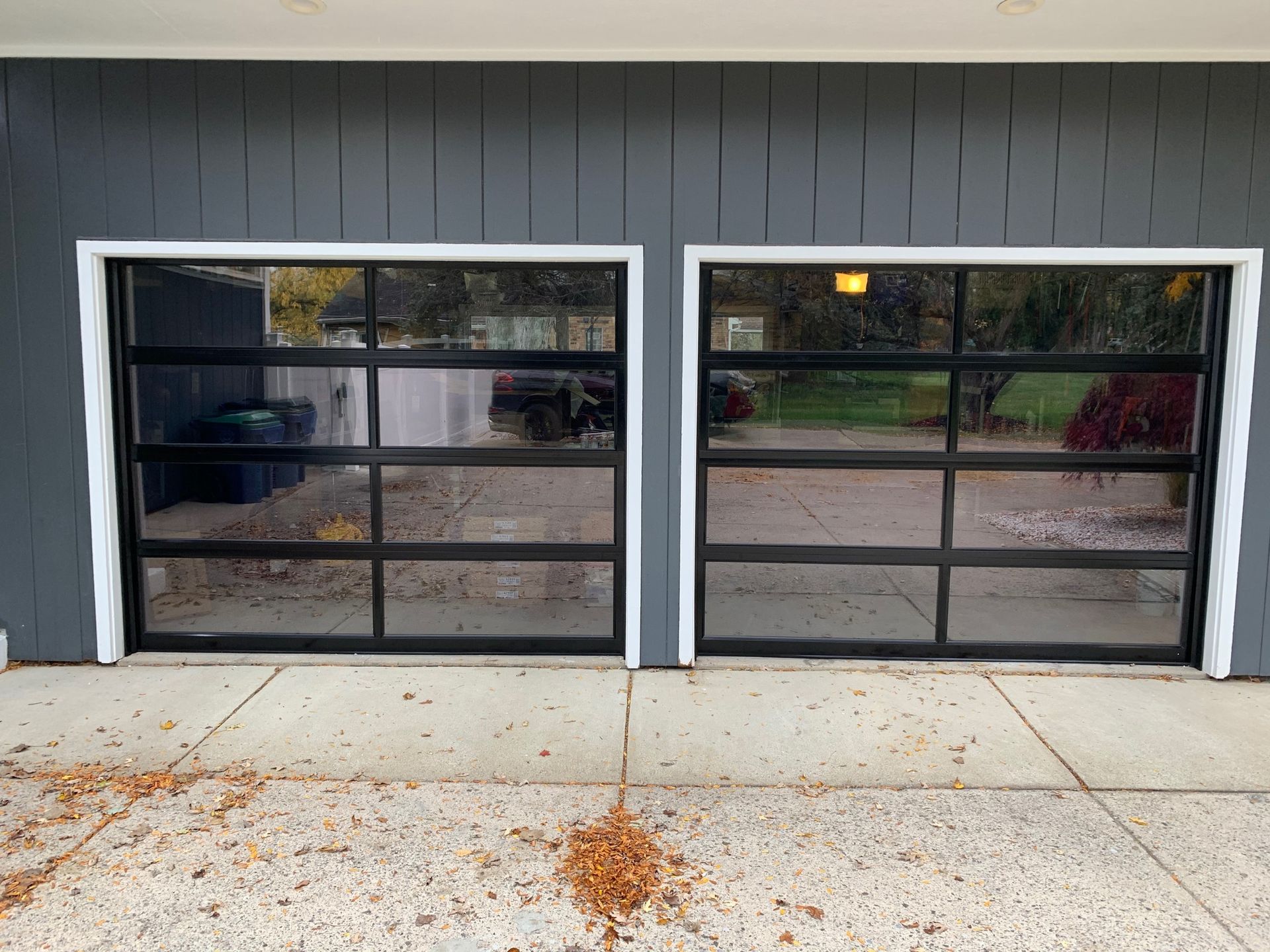 Two garage doors with black frames and tinted glass, set in a gray house with white trim.