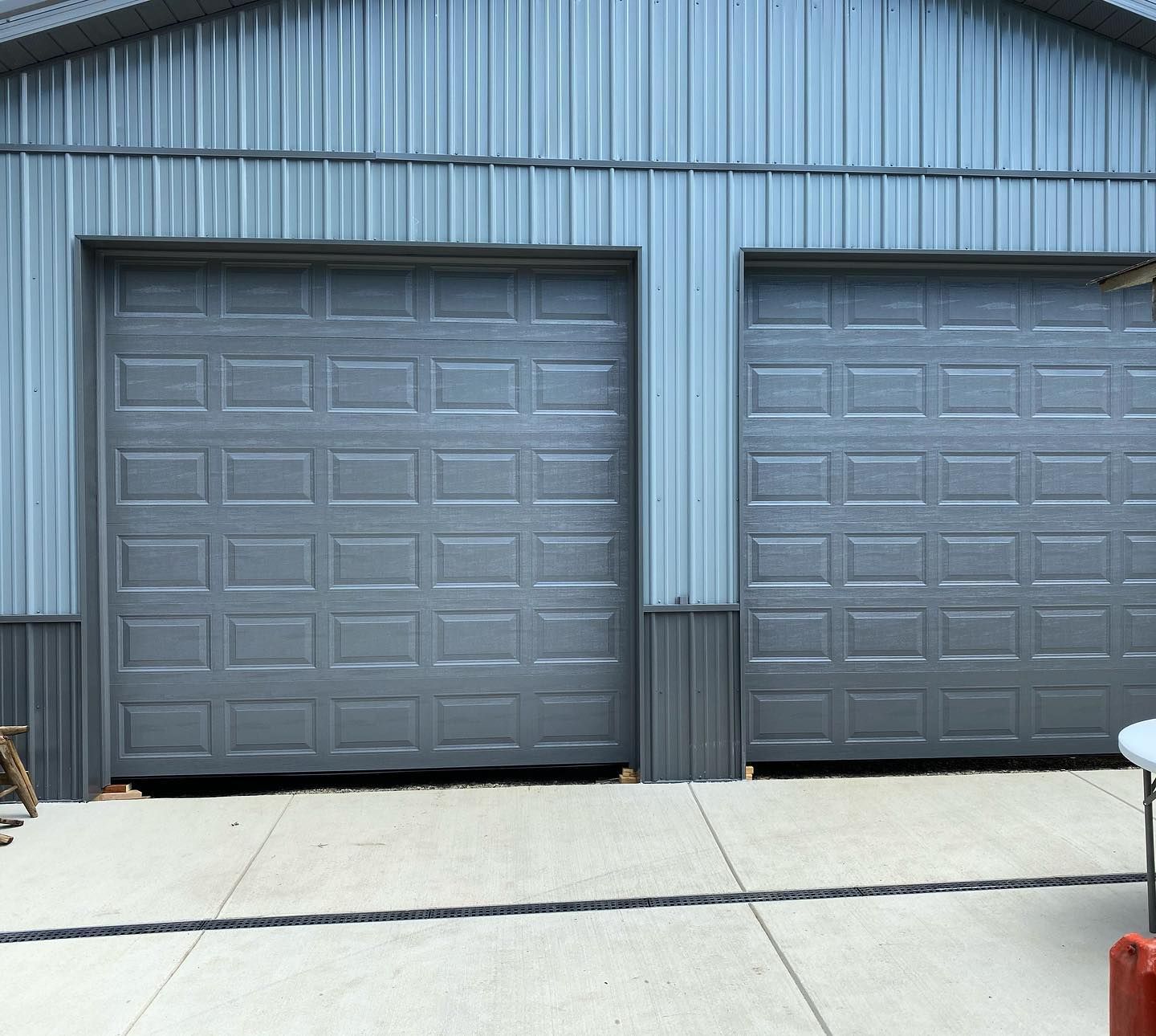 Two closed gray garage doors on a blue metal building. Concrete driveway in front.