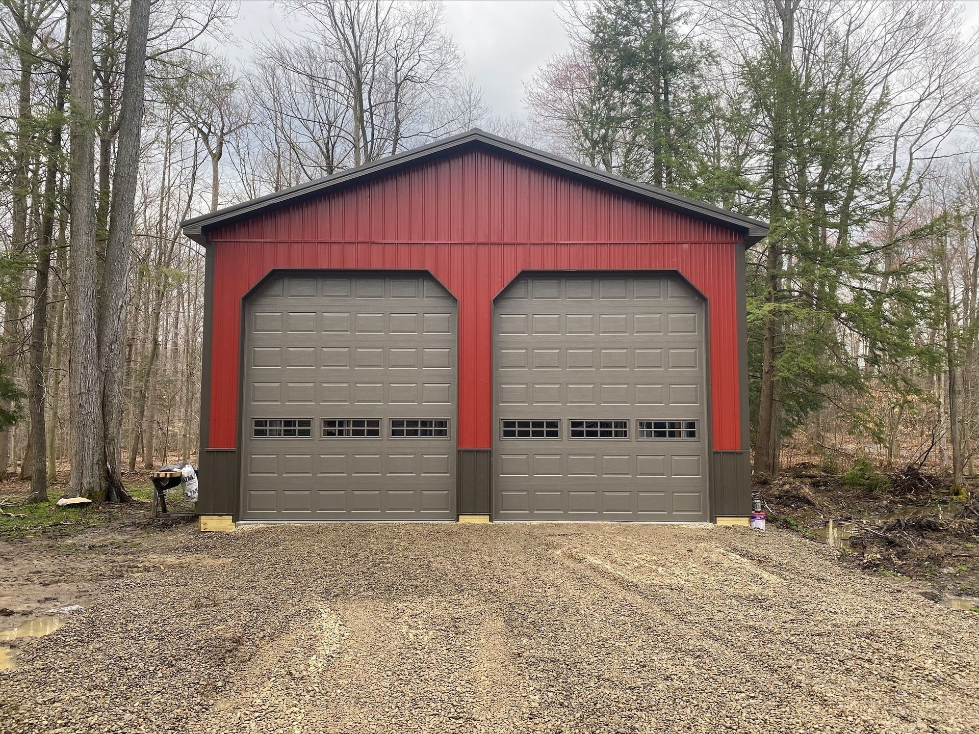 Red and brown two-car garage with two gray garage doors in a wooded area.