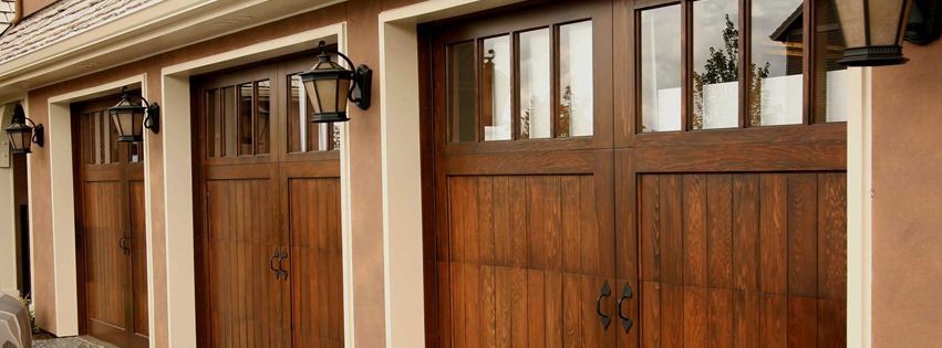 Three brown garage doors with rectangular windows, tan frames, and black lanterns.