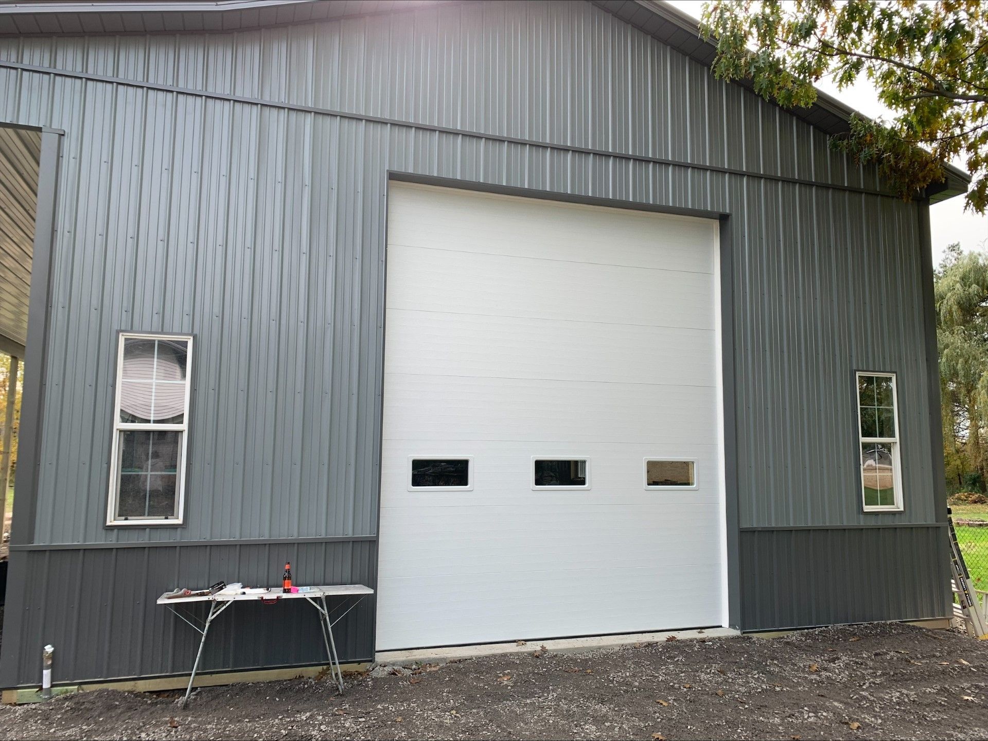 Gray metal barn with a large white garage door and two small windows.