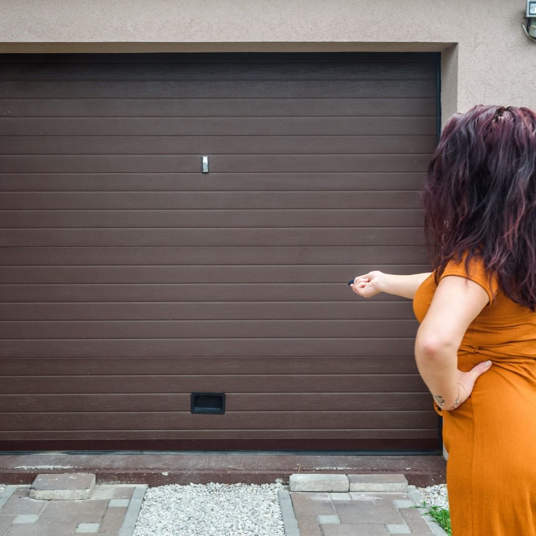 Woman in orange dress points toward a brown garage door.