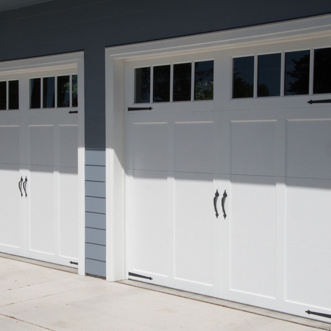 White garage doors with black handles and windows, side by side, in bright sunlight.