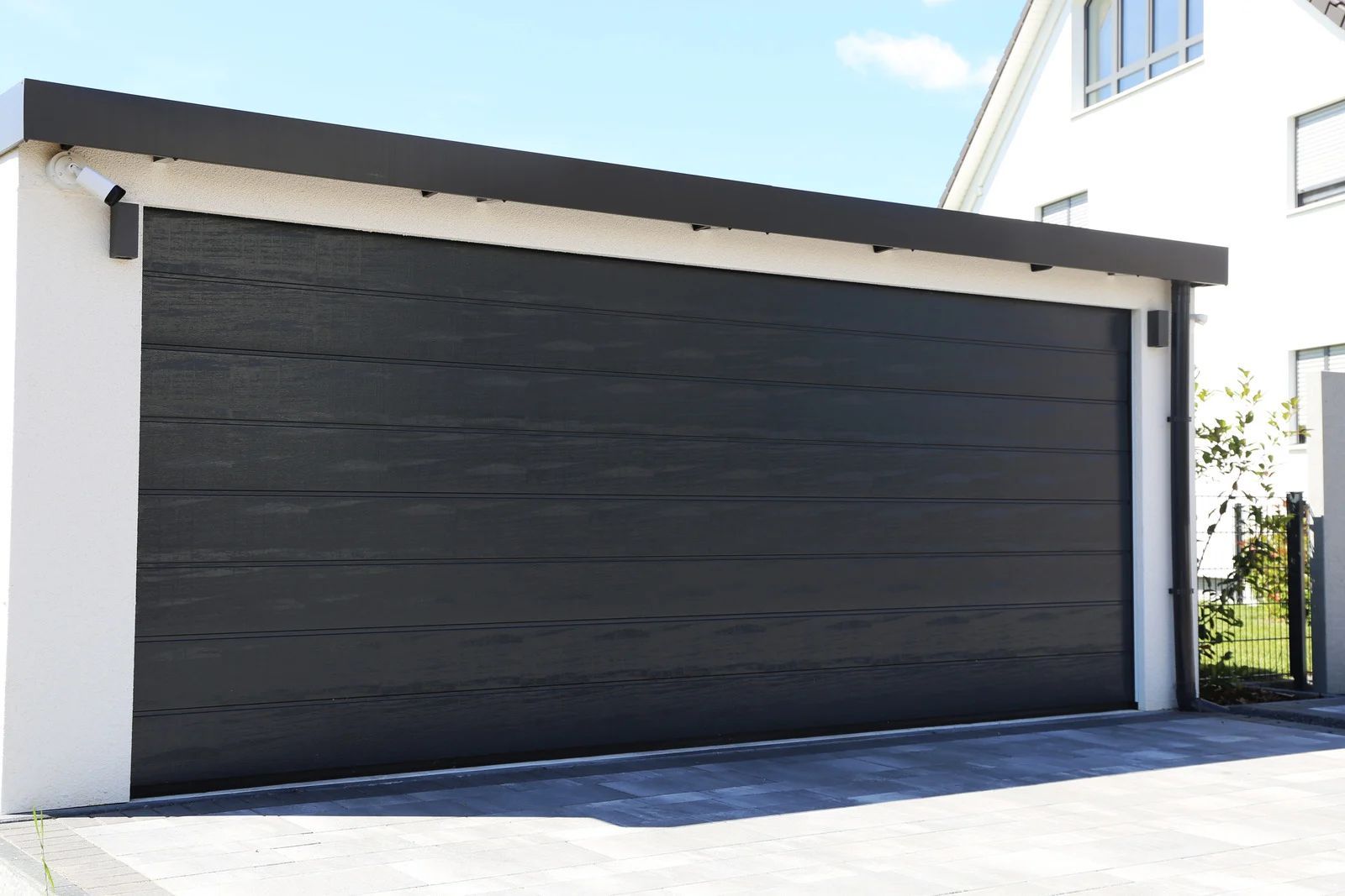 Dark gray garage door on a white building with a black awning; sunny day.